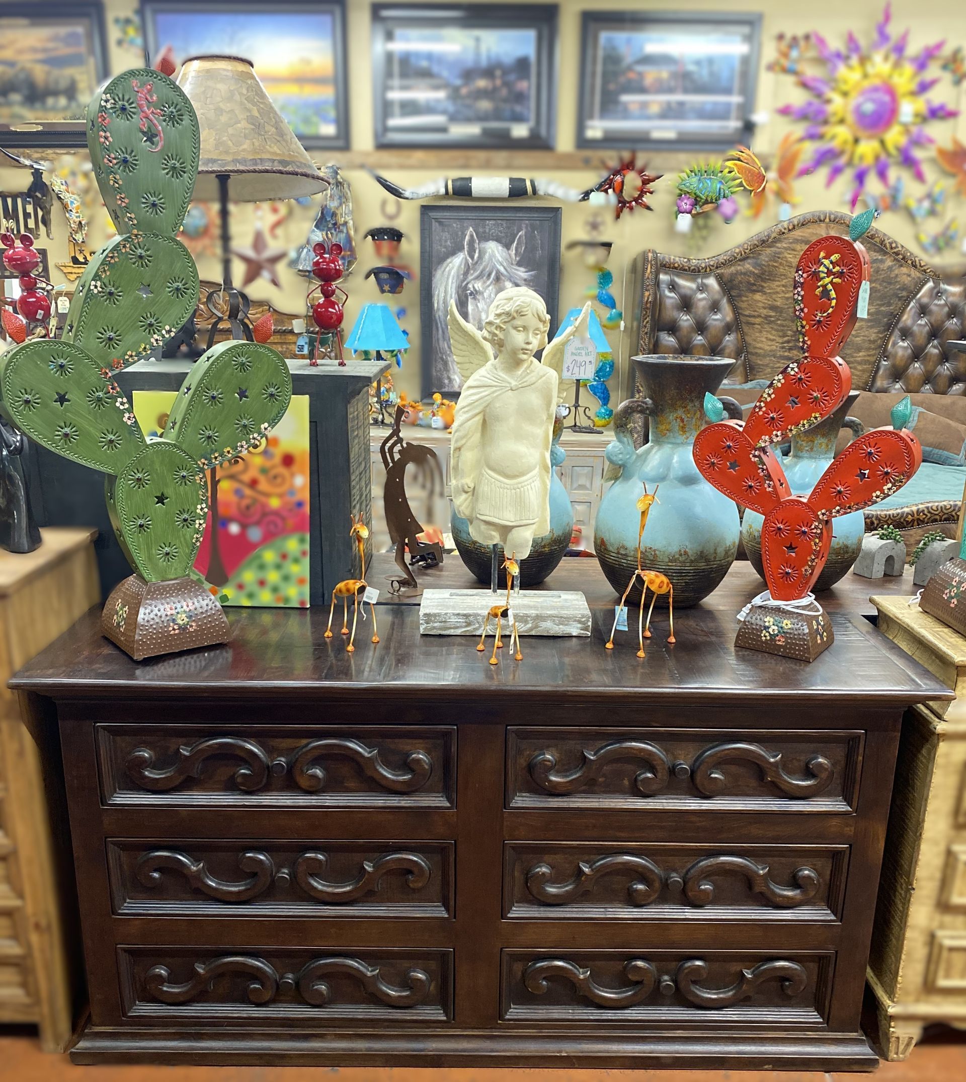 Wooden dresser with various decorative items on top, including cactus sculptures and a cherub statue. Store interior.