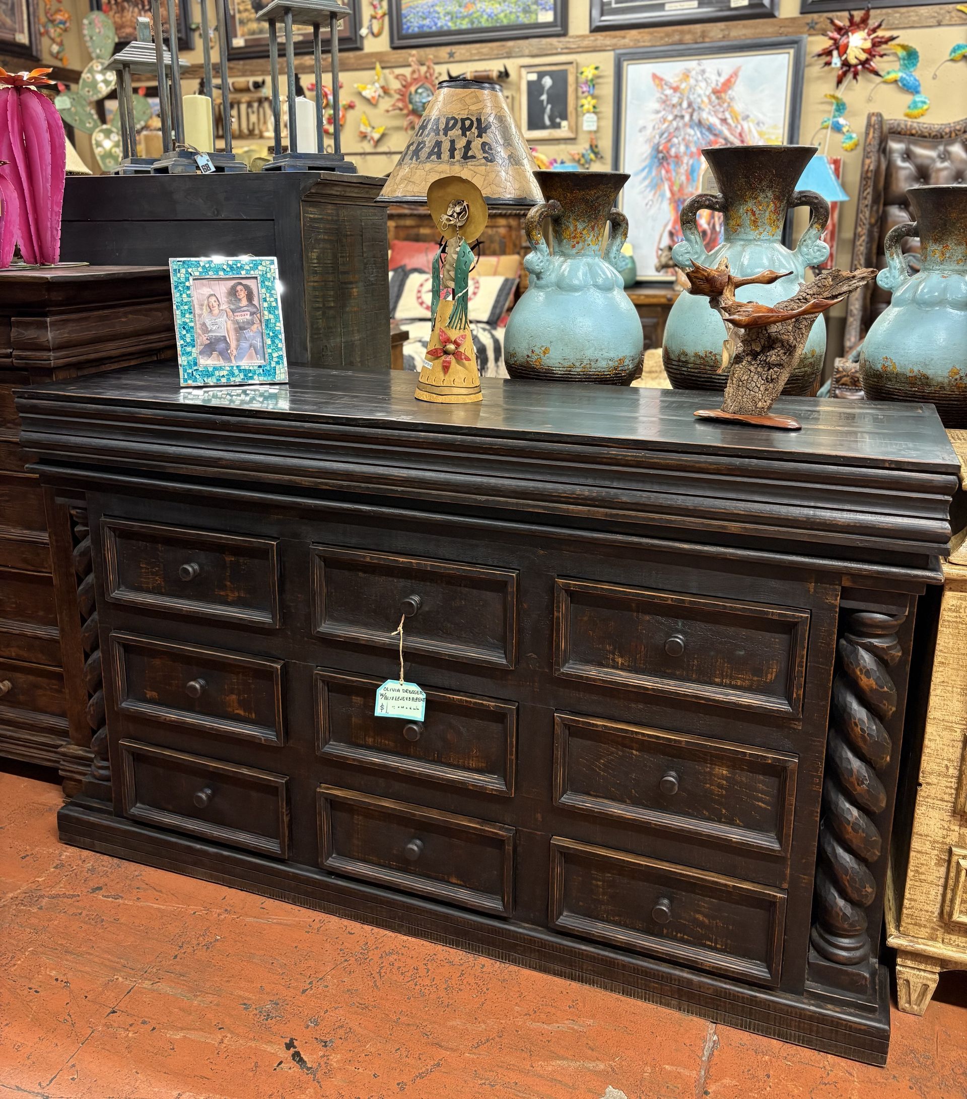 Dark wood cabinet with carved details, topped with vases and decorations in a shop setting.