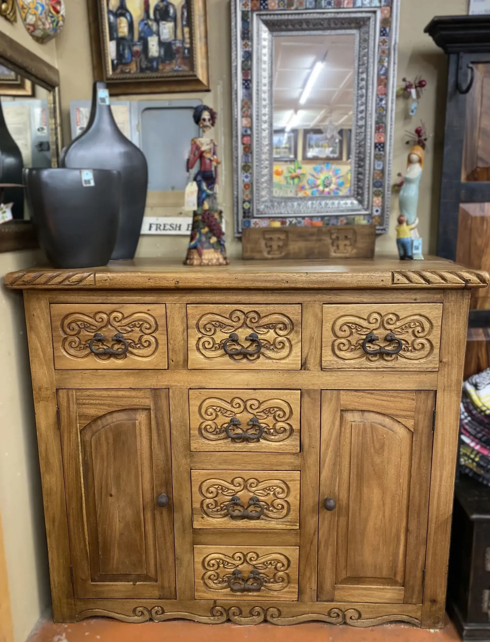 Wooden cabinet with carved details and decorative items on top, including vases, a statue, and a mirror.