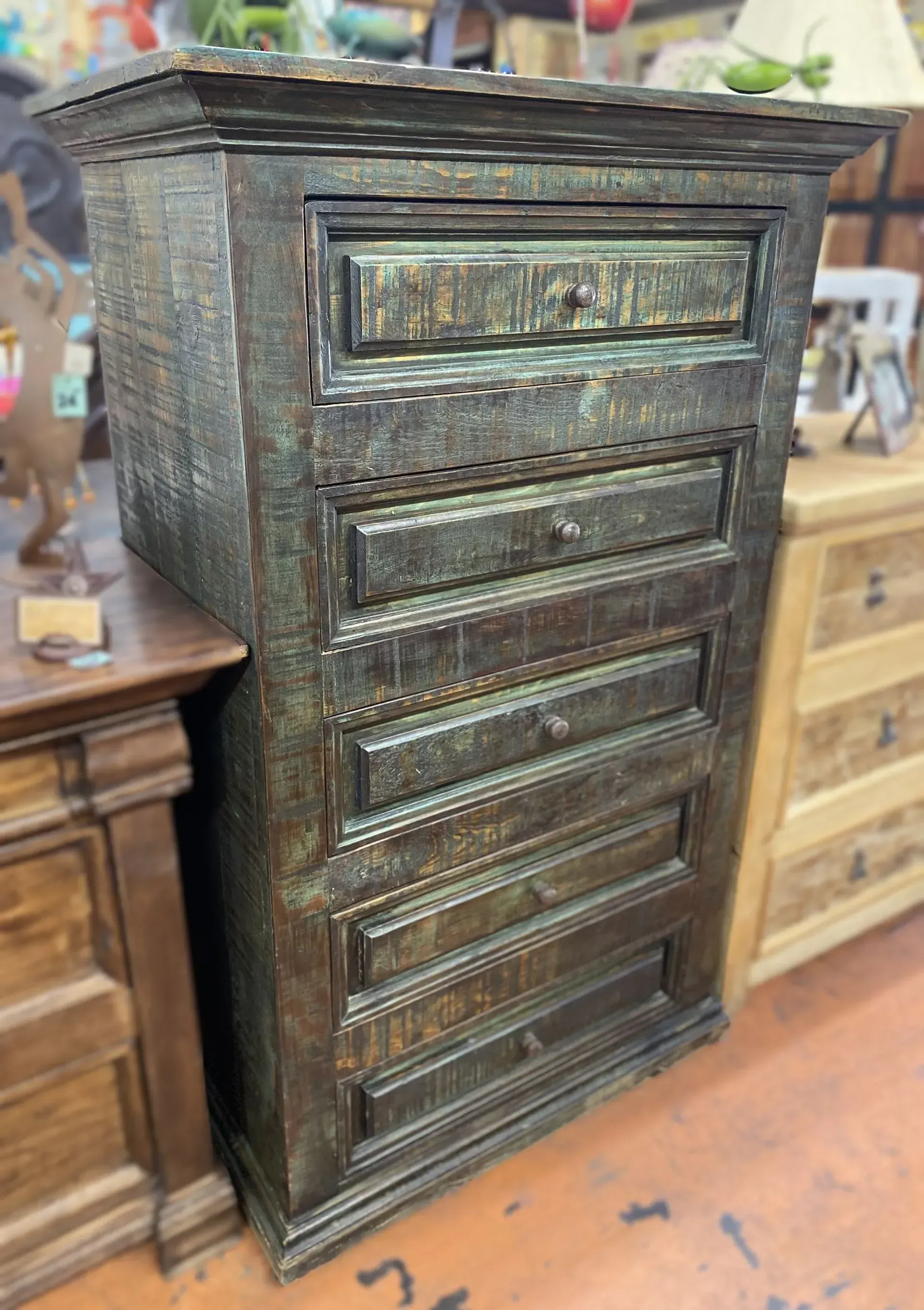 Tall, weathered, wooden chest of drawers with six drawers and a small top drawer. Dark green and brown color with a rustic finish.