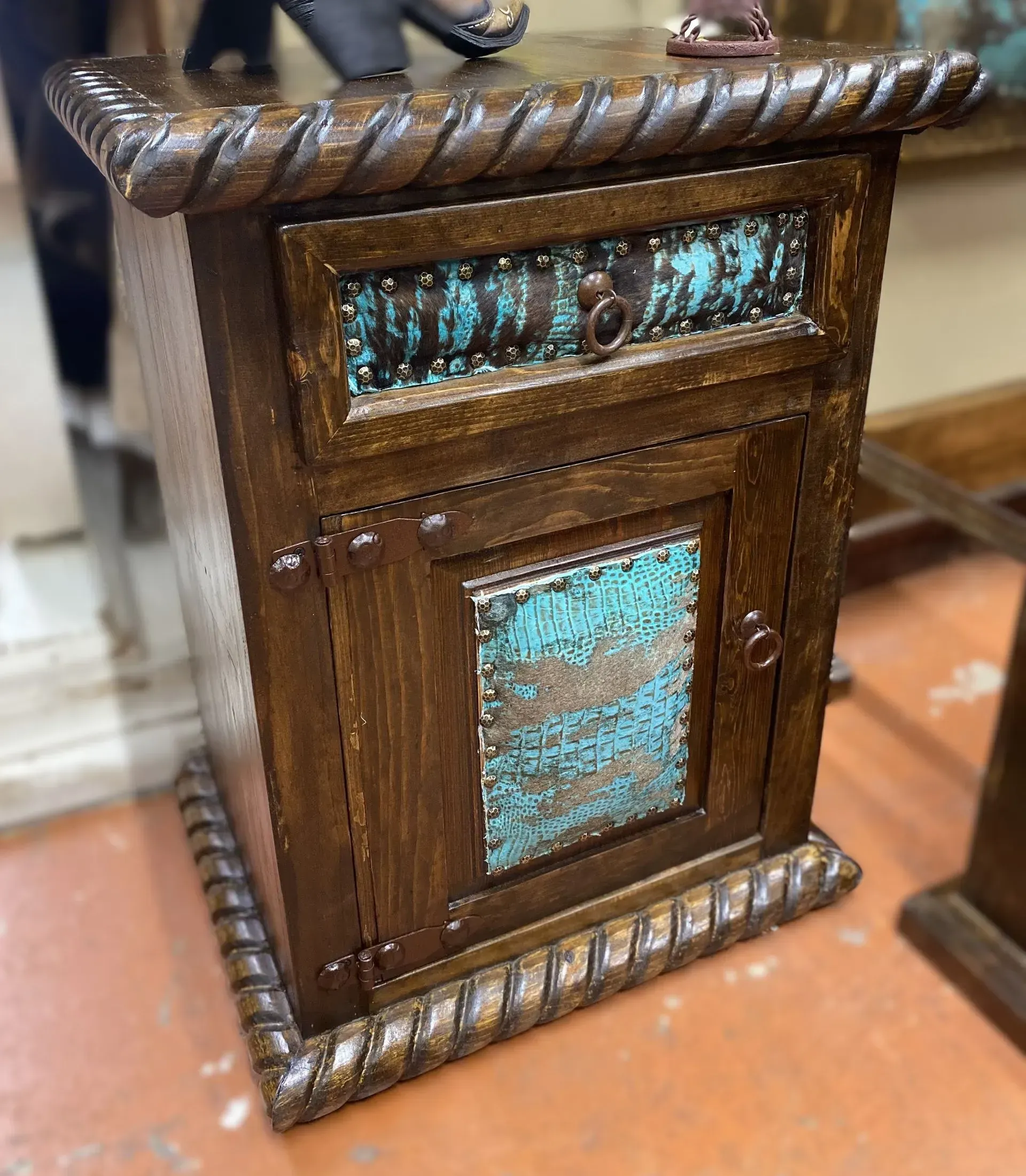 Dark wooden nightstand with turquoise-colored accents, a drawer, and a cabinet door, in a room.