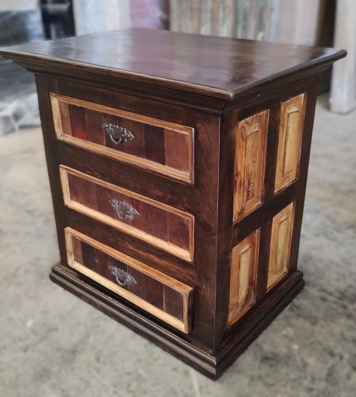 Wooden nightstand with three drawers, stained dark brown with lighter wood accents. Antique-style hardware.