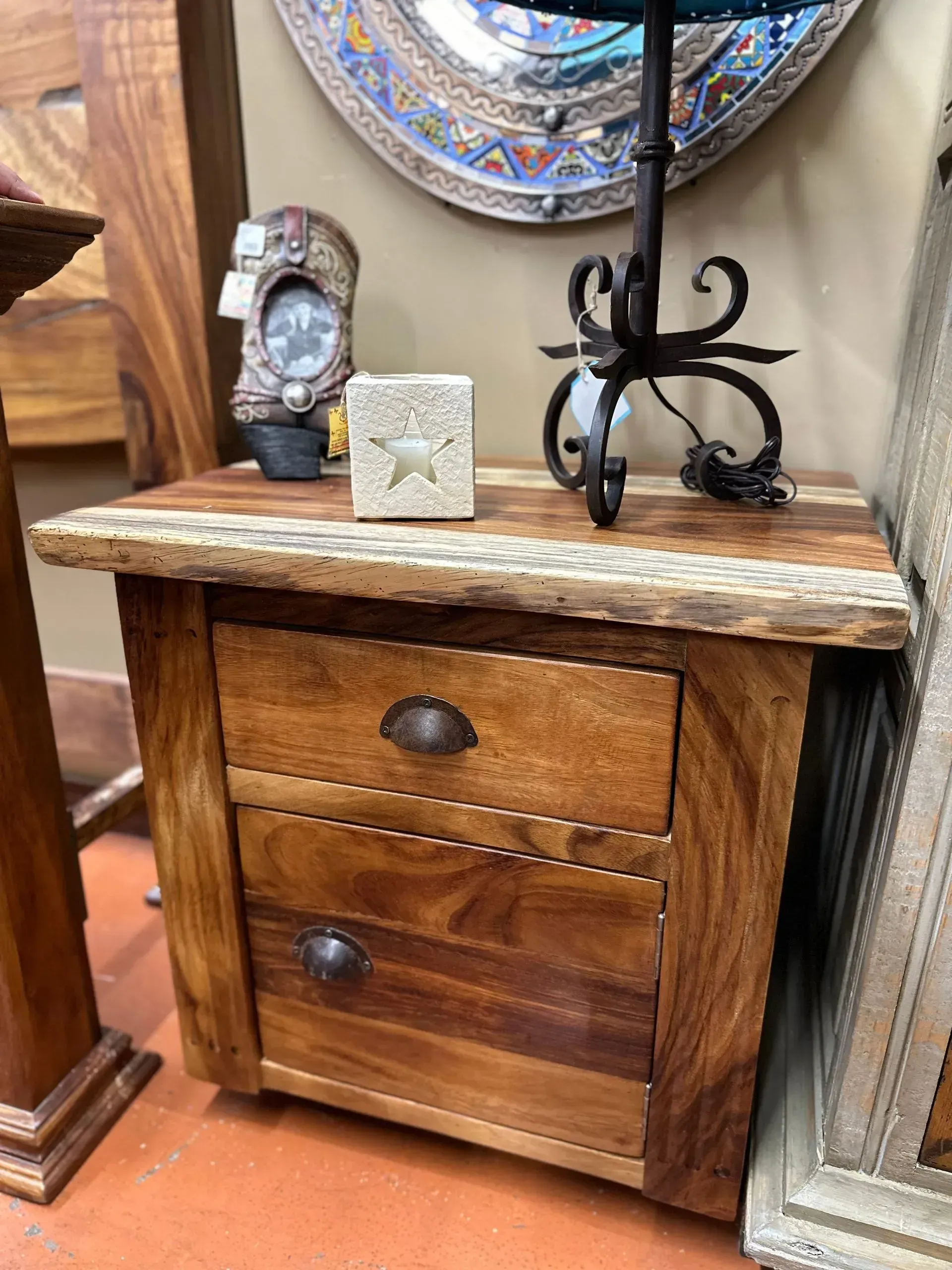 Wooden nightstand with two drawers and a rustic design, topped with a lamp and a small decorative block.