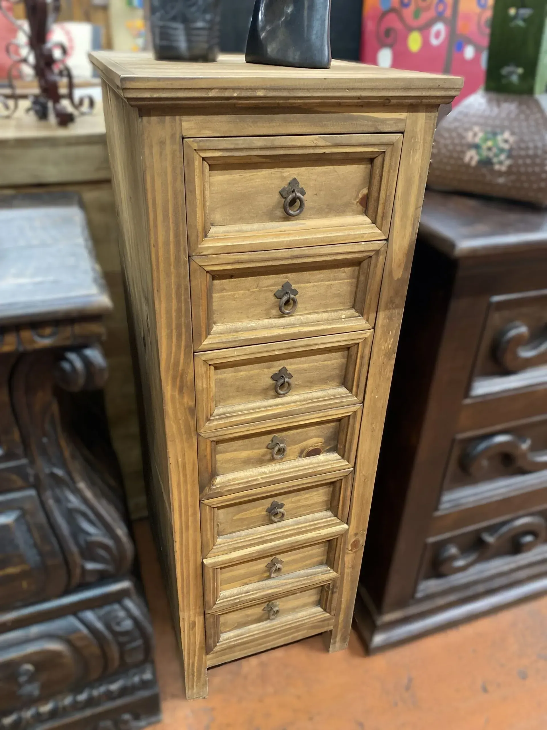 Tall, narrow wooden cabinet with seven drawers, ornate handles, and a slightly weathered appearance.