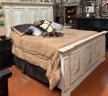 A rustic, white-washed wooden bed frame and headboard. The bed is made with a tan and brown comforter and decorative pillows.