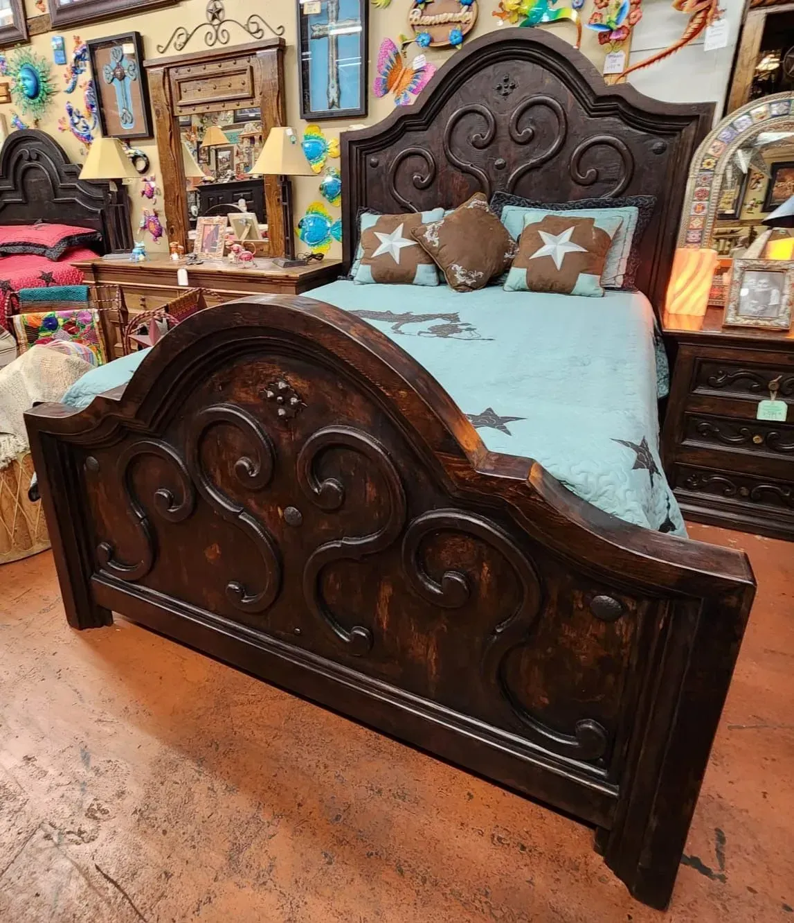 Dark wood bed with ornate carvings, two star pillows, and a light blue quilt. The bed is in a store with various decorations.