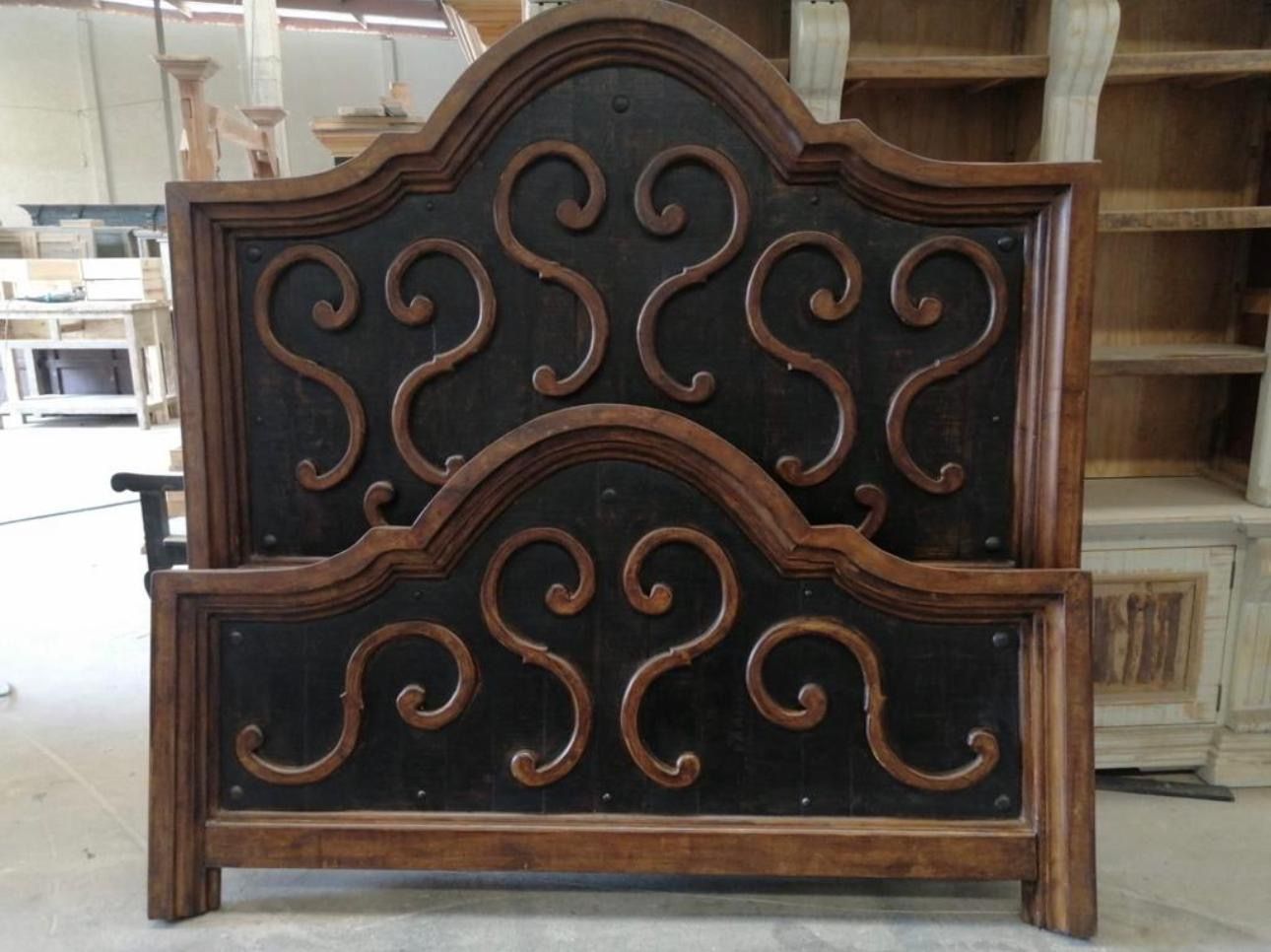Ornate wooden bed frame with dark center panel and scrollwork, against a cluttered workshop backdrop.