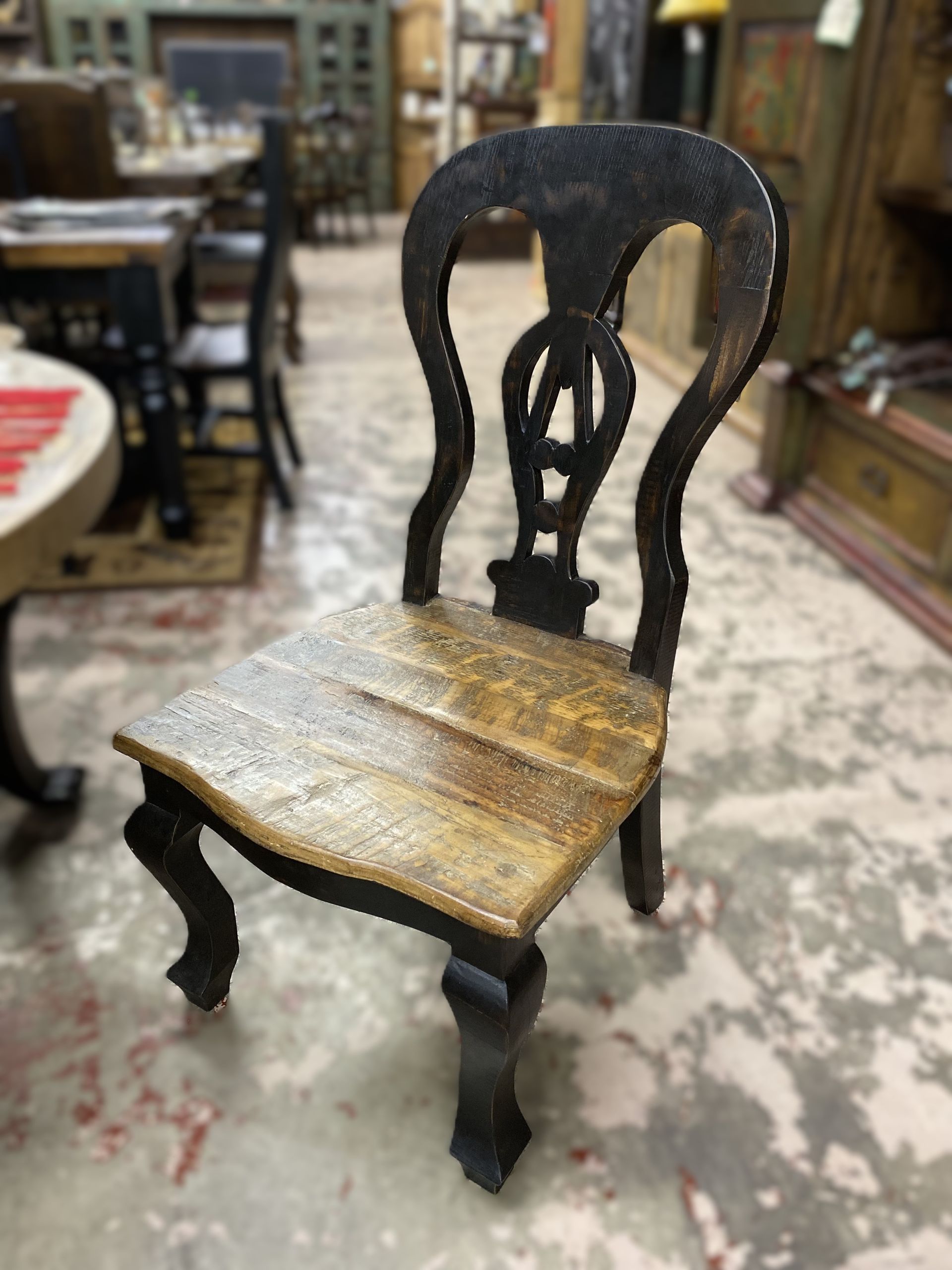 Wooden antique chair with a black frame and light brown seat, set in a furniture store.