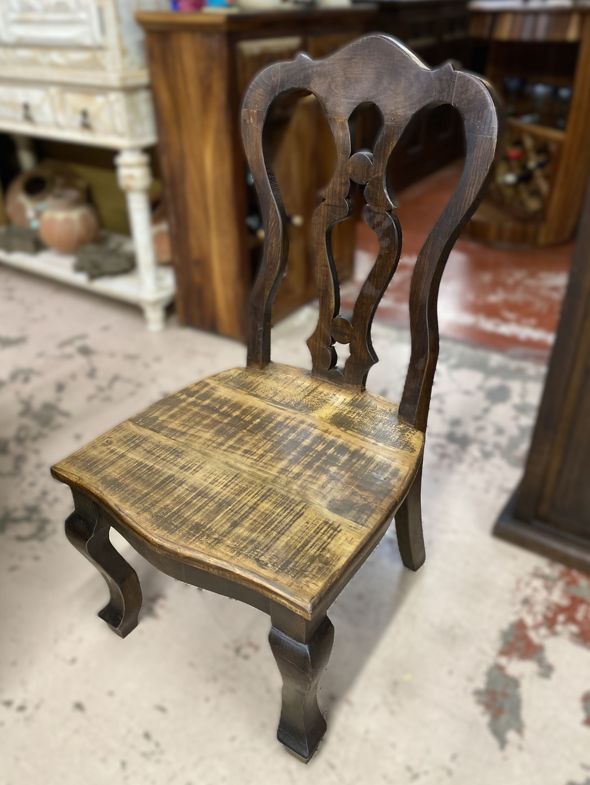Wooden chair with a carved back and distressed, light-colored seat. Dark brown finish.