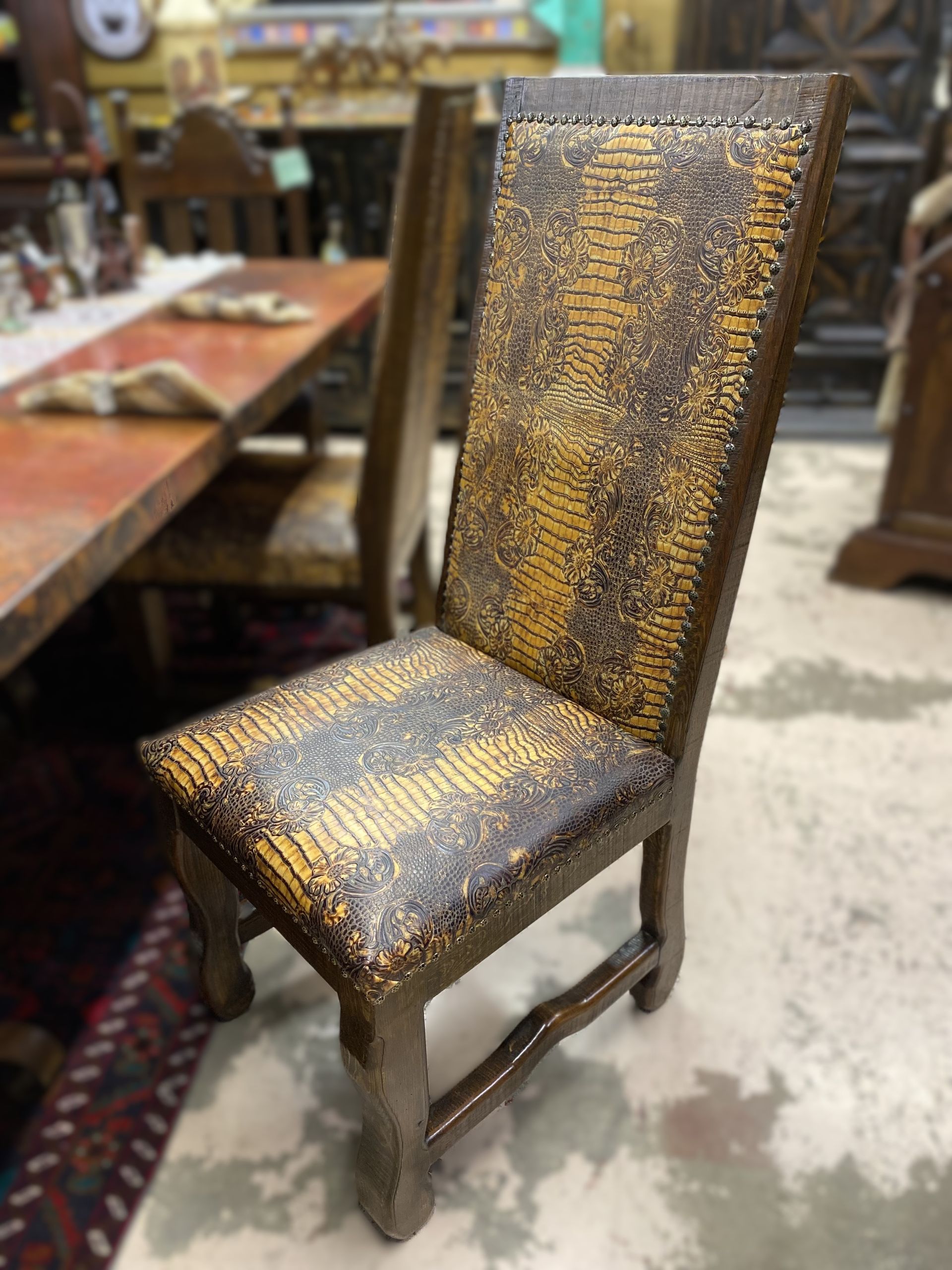 Wooden chair with tall back and seat upholstered in a textured, reptile-patterned material, in a room with other furniture.