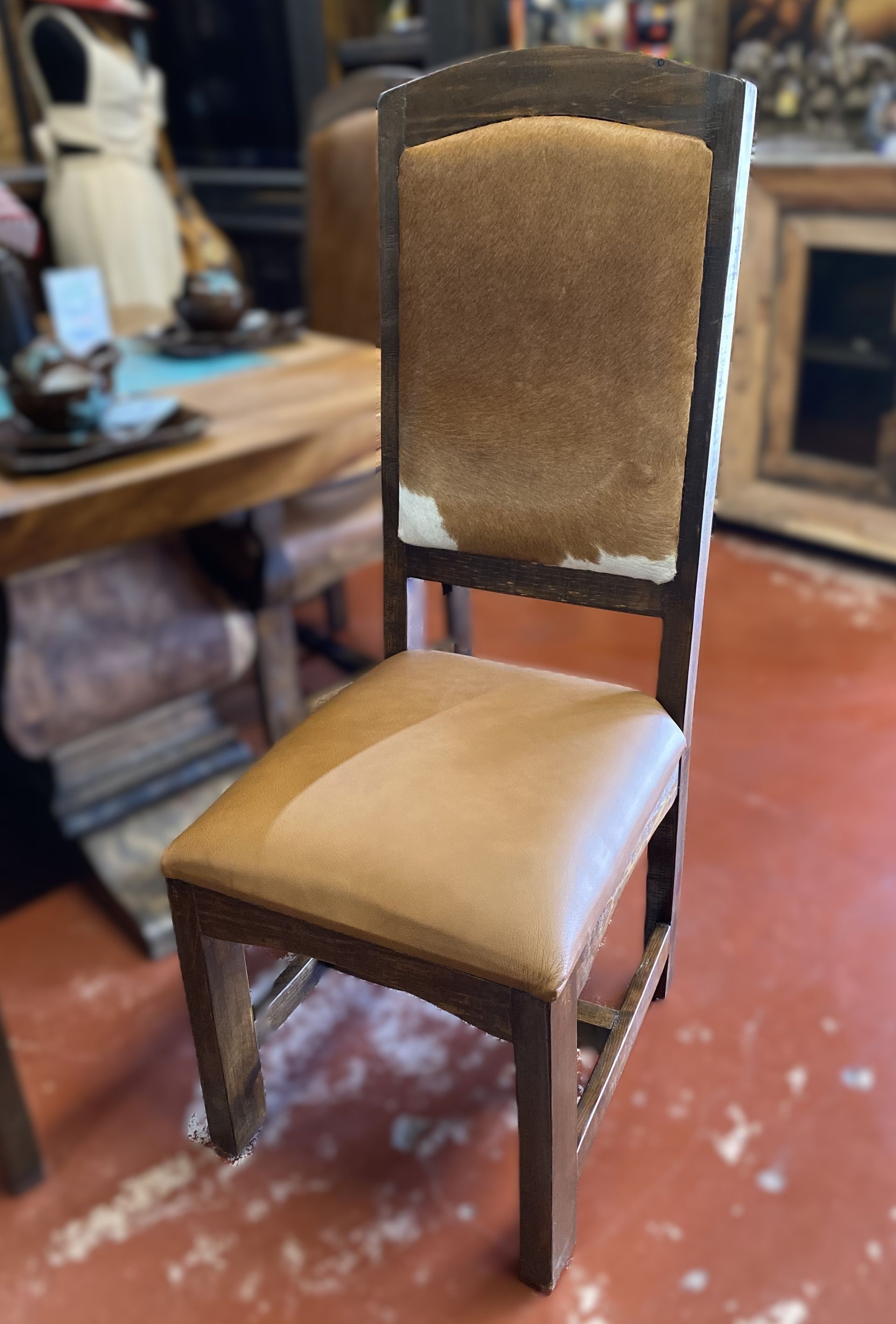 Wooden chair with a light brown leather seat and a cowhide backrest, in a rustic setting.
