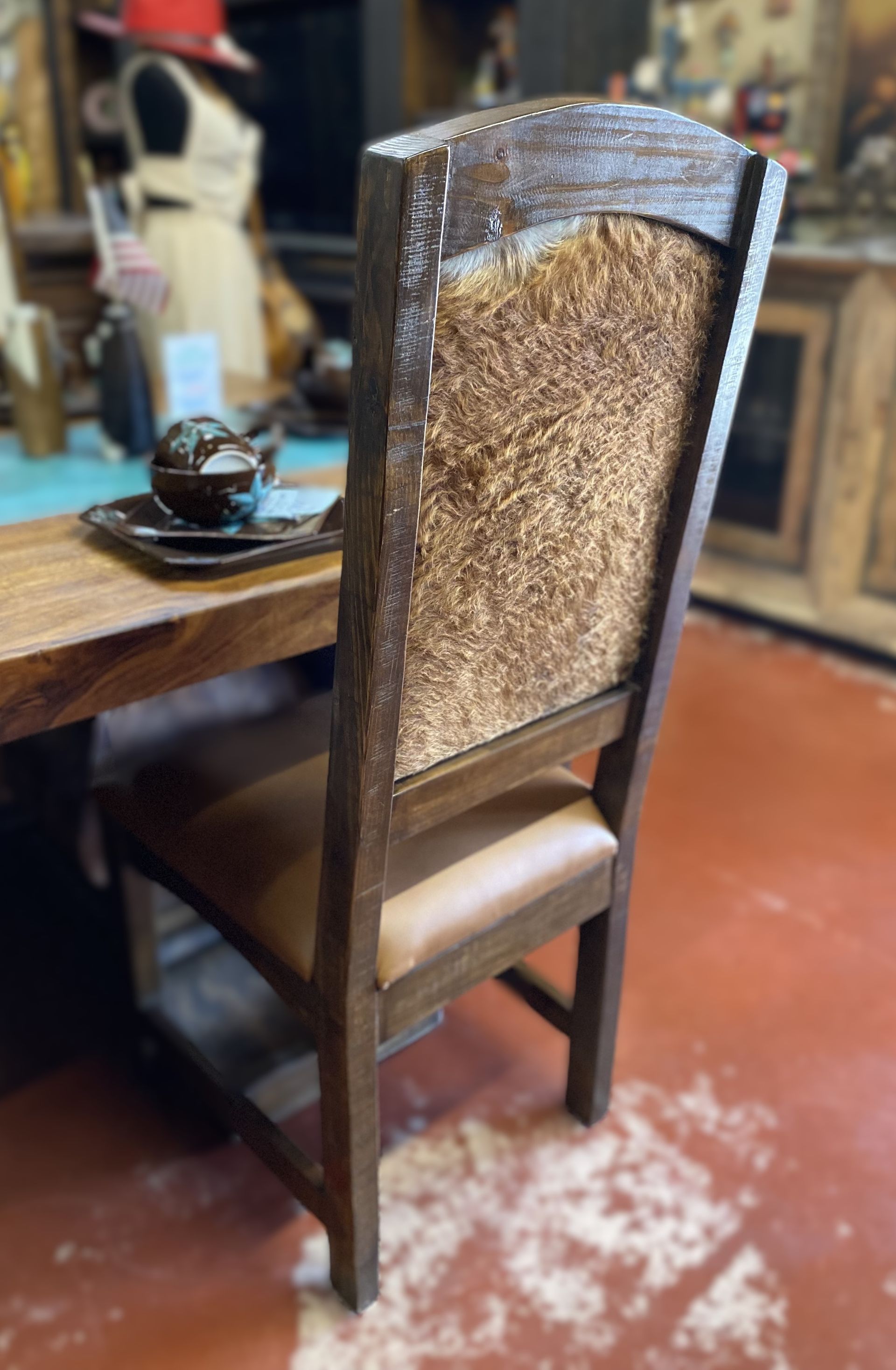 A wooden dining chair with a brown leather seat and a textured back, in a room with a wooden table.