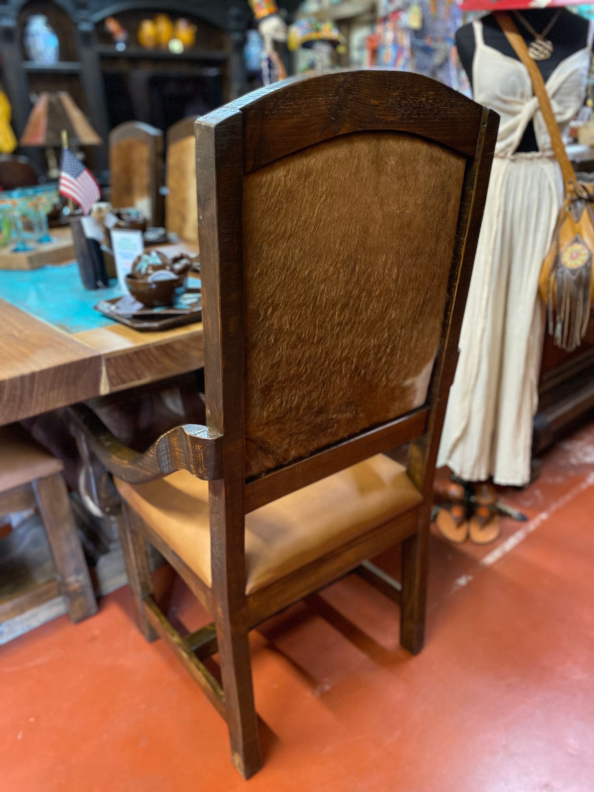 Wooden chair with a brown cowhide back and tan leather seat, placed near a table in a store.