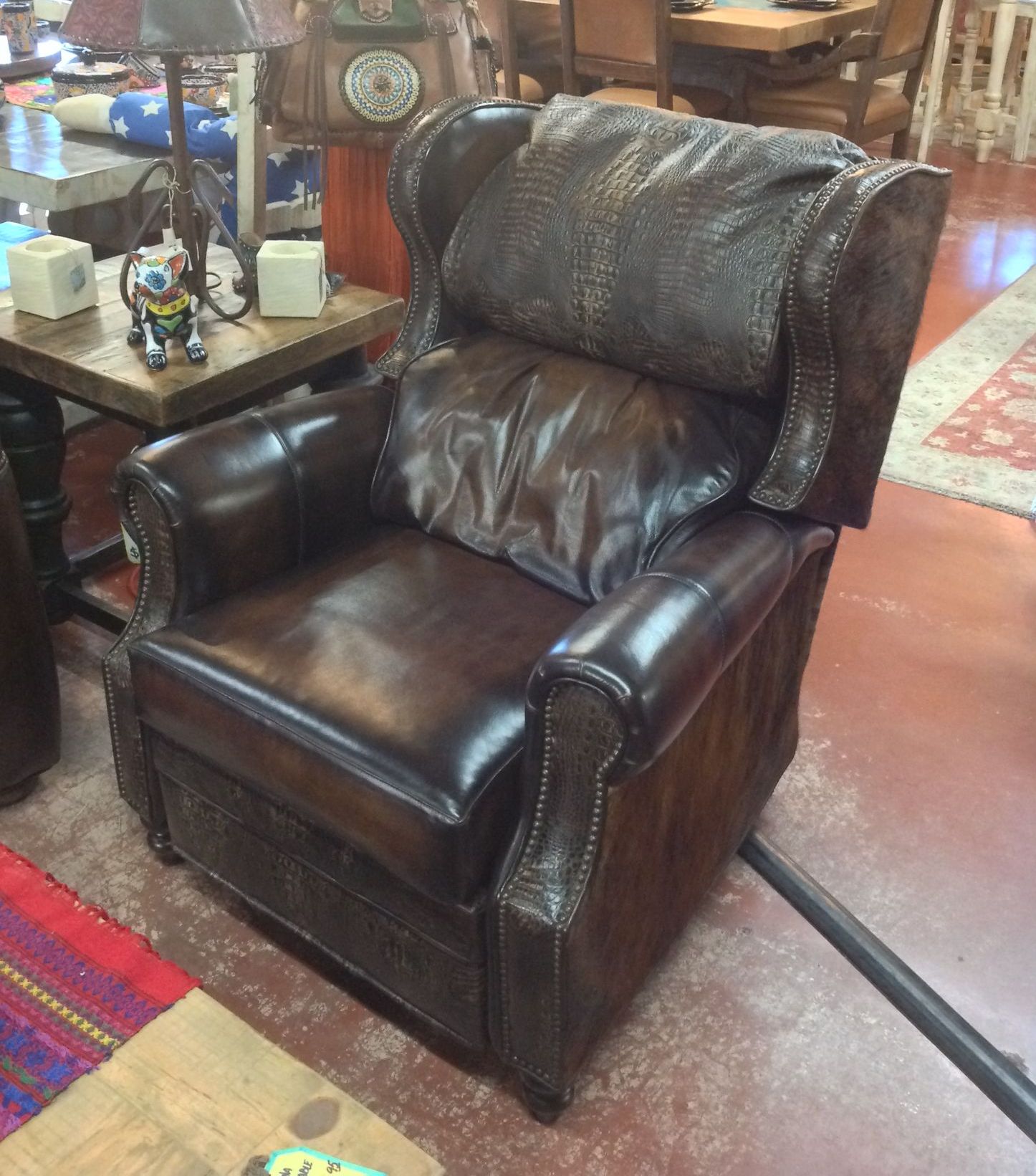 Brown leather wingback armchair in a rustic setting, with a side table and rug.