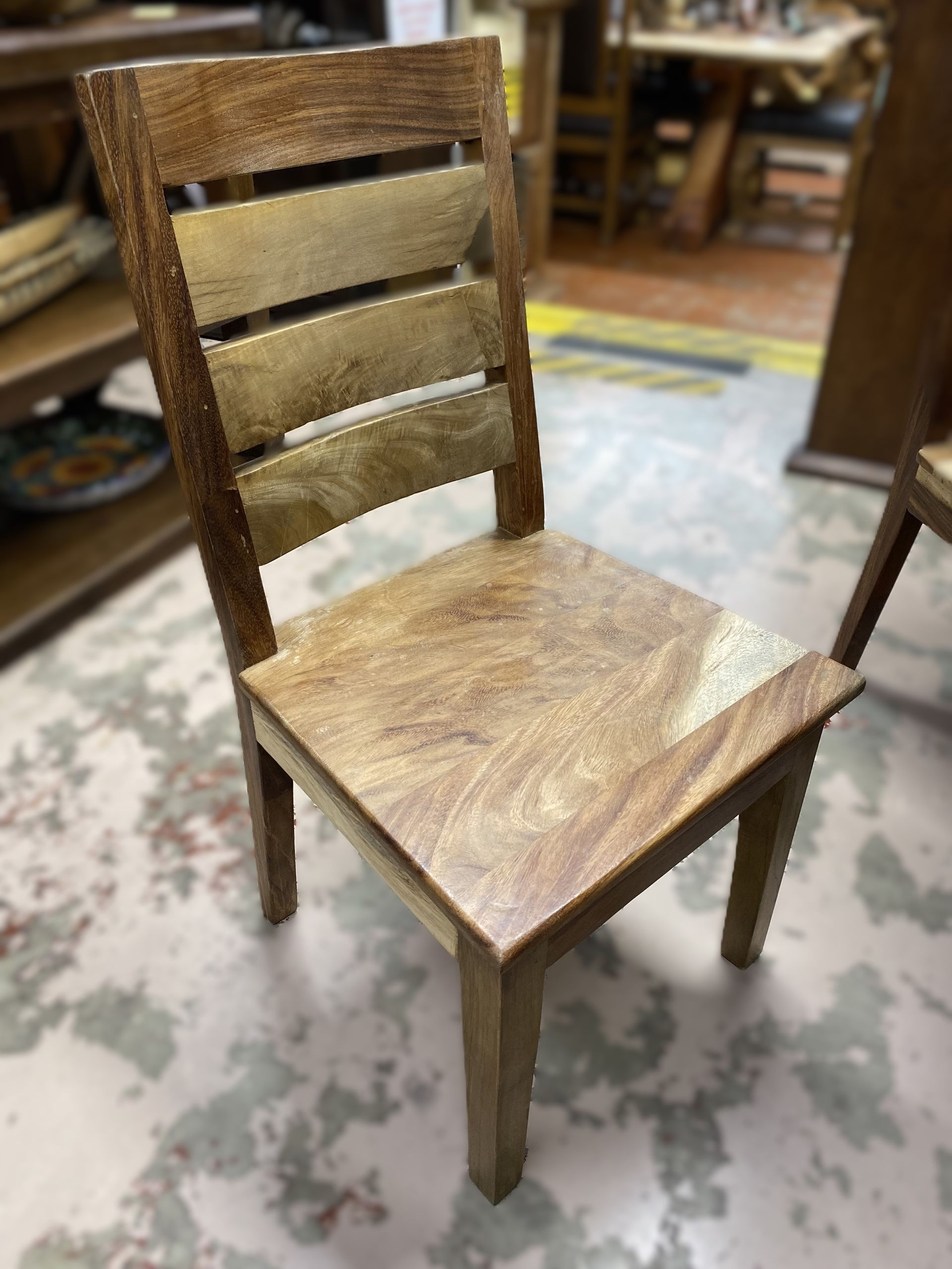 Wooden chair with a light brown seat and a back composed of horizontal planks. The setting appears to be a shop.