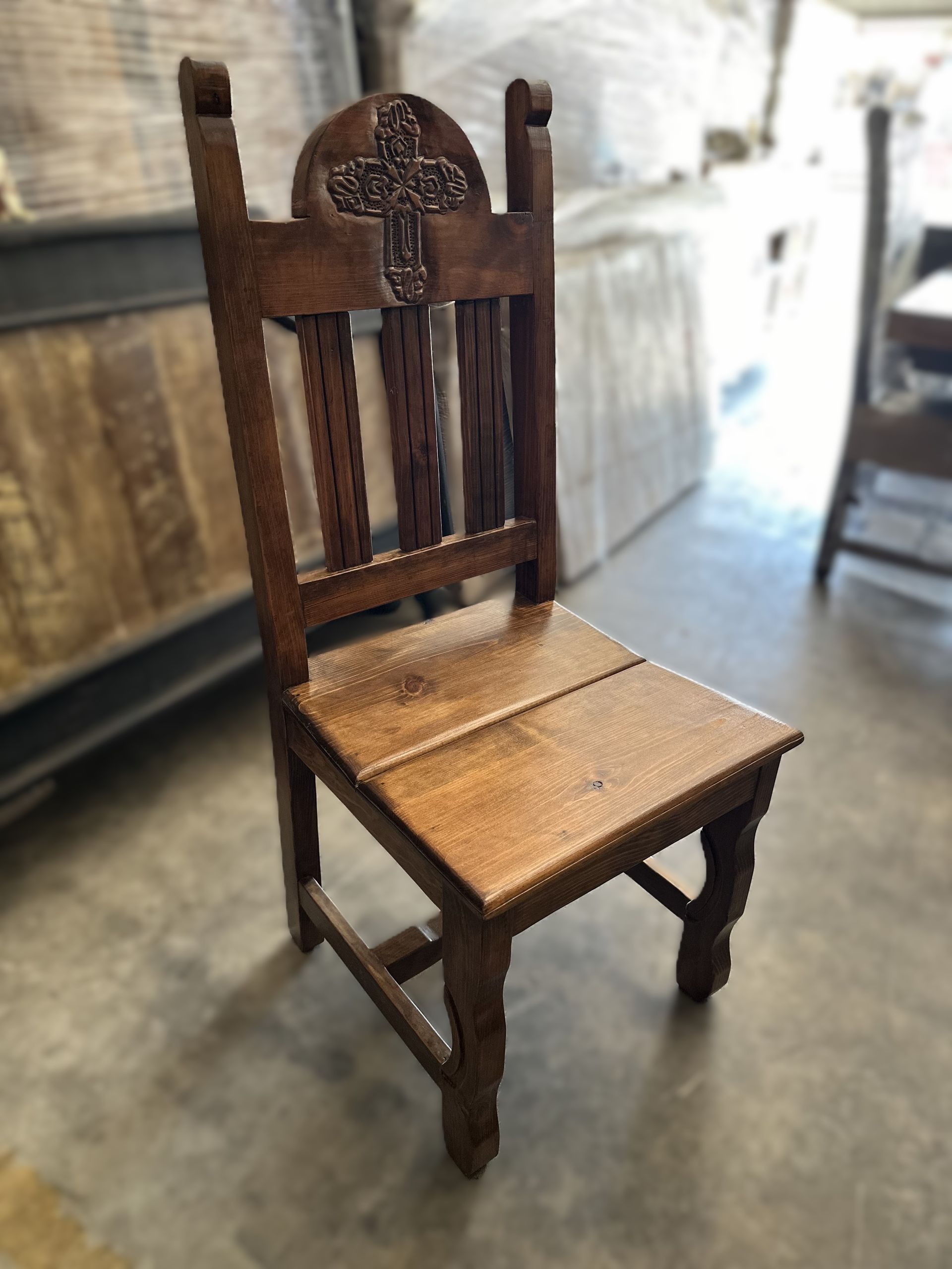 Wooden chair with a carved back featuring a cross design, set in a rustic setting.