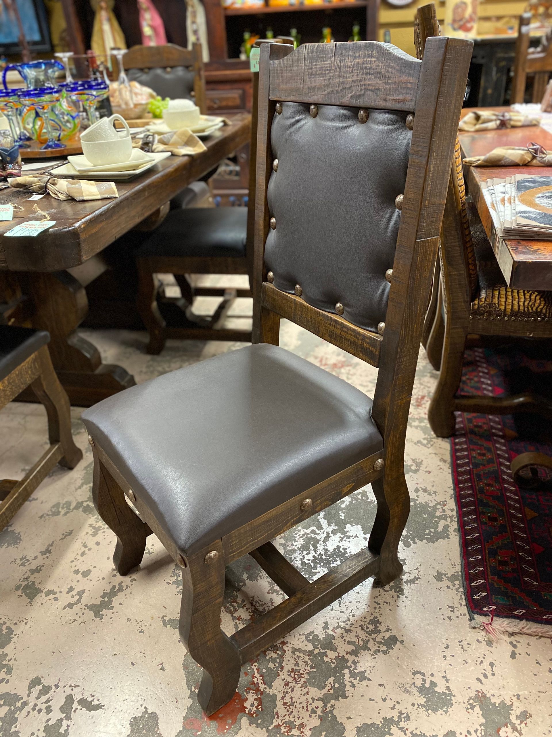 Dark wooden chair with a gray leather seat and back, studded with brass tacks. Set in a room with a dining table.