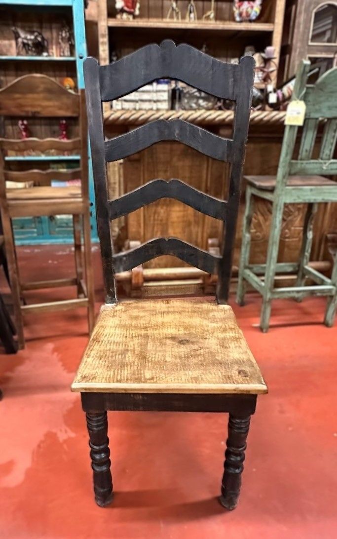 Wooden chair with a black, ladder-back style upper and a natural, weathered seat. The legs are turned, and the floor is red.