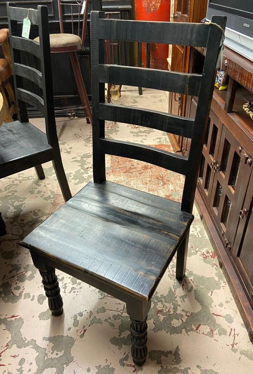 Black wooden chair with ladder back and turned legs, set in a room with other furniture.