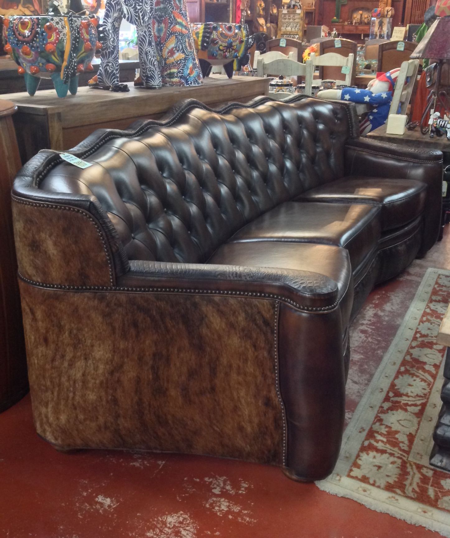 Curved, dark brown leather sofa with button tufting and cowhide accents in a furniture store.