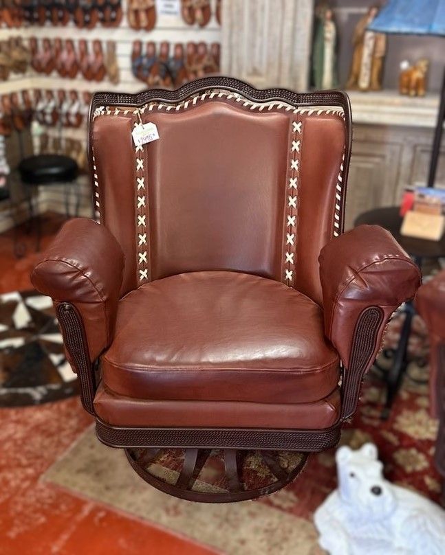 Brown leather swivel chair with light stitching, ornate carved detailing, displayed in a shop.