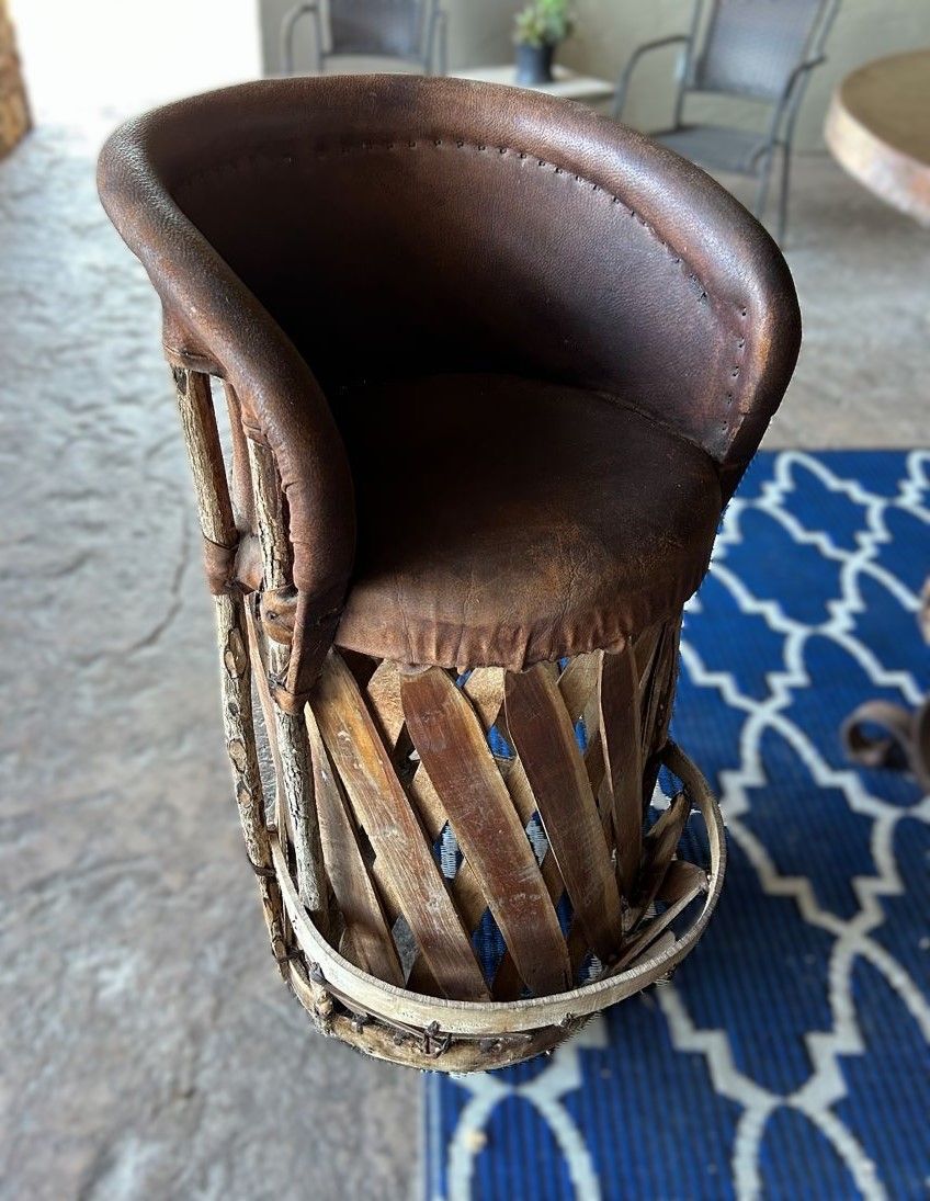 A leather and woven wooden chair, outdoors. It has a dark brown leather seat and backrest, and a light brown woven base.