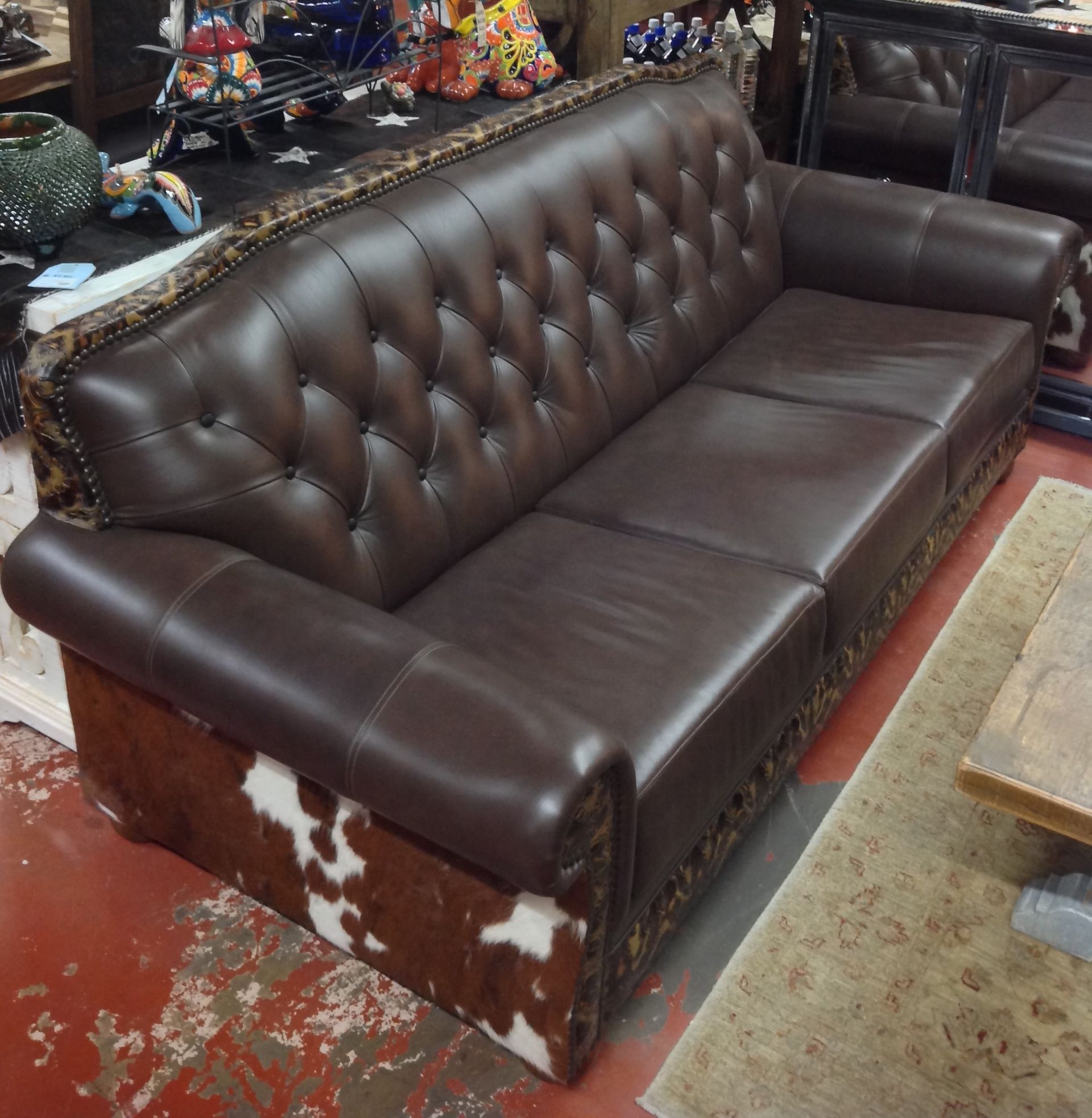 Brown leather sofa with tufted back and cowhide detailing on the base.