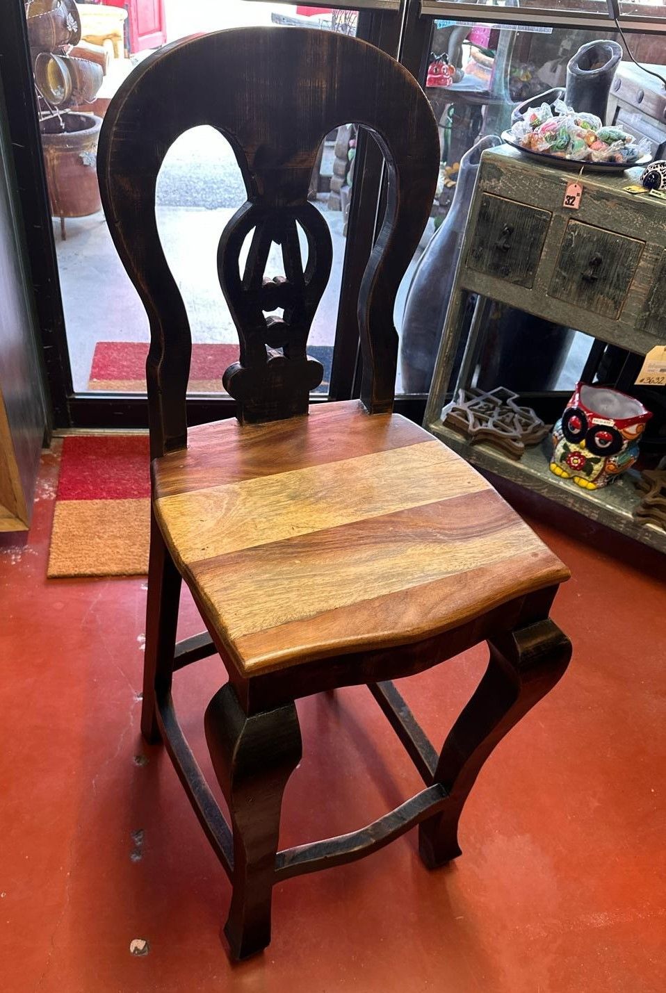 A dark-wood chair with a light-wood seat and a decorative back, sitting on a red floor.