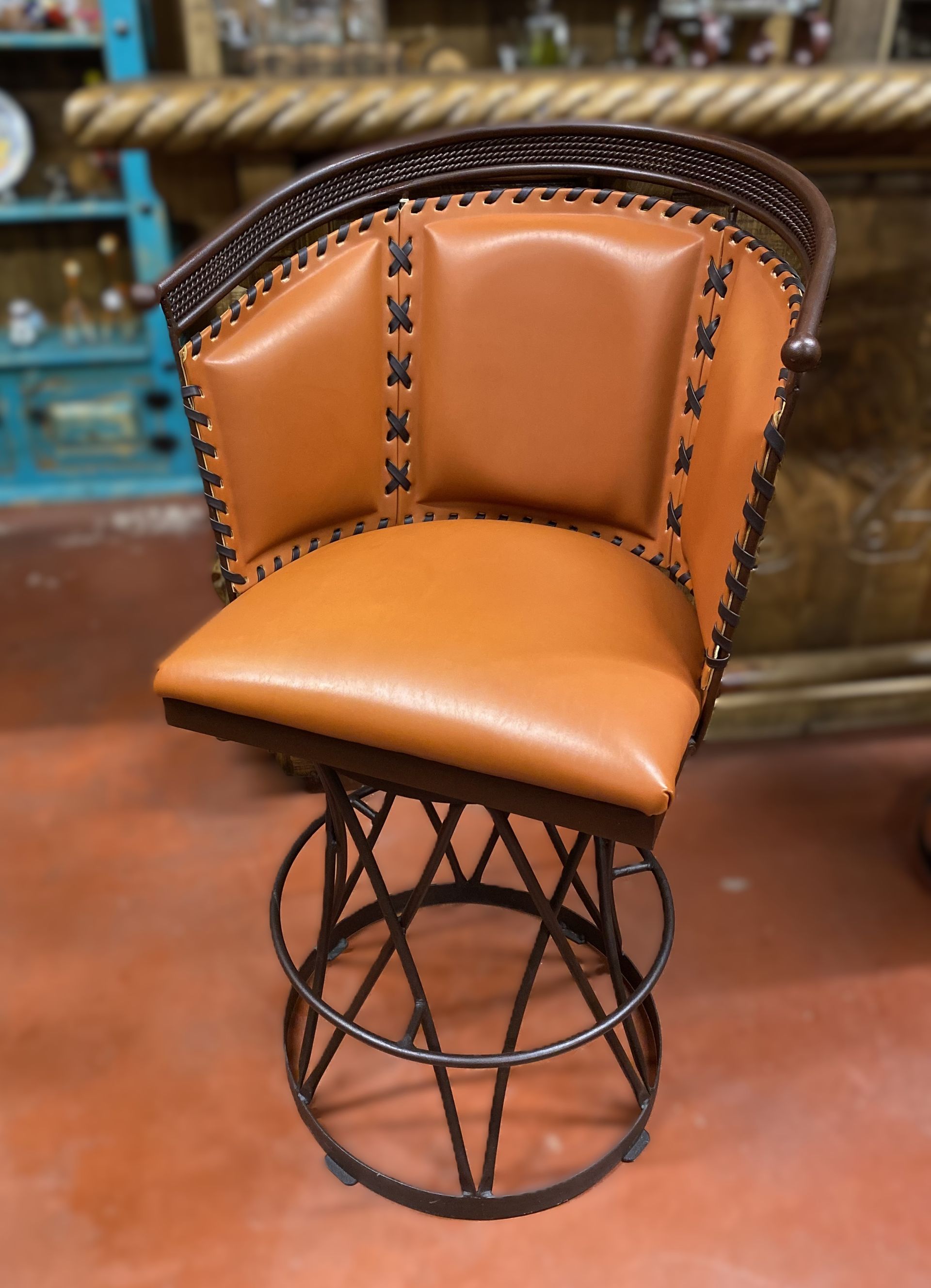 Brown leather bar stool with dark metal frame. The stool has a stitched backrest and a swivel seat.
