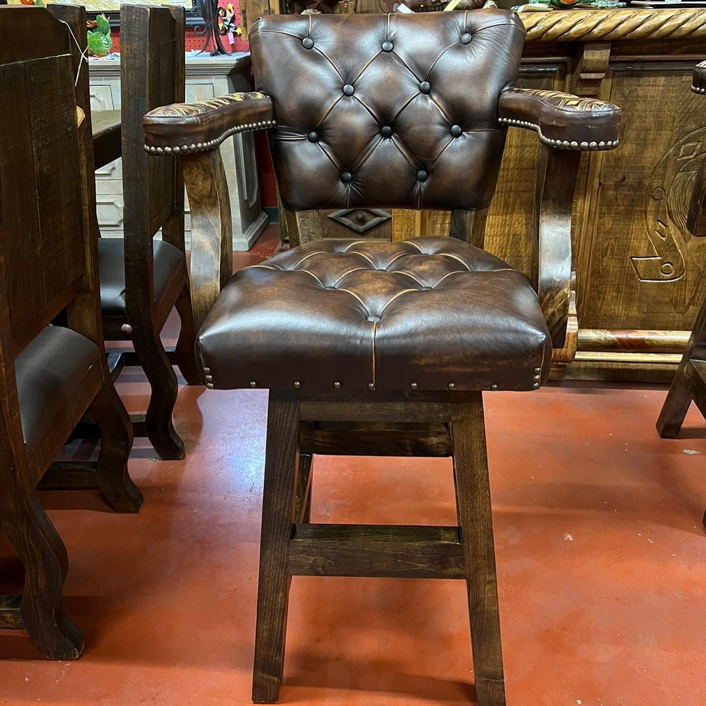 Brown leather barstool with studded details and a tufted seat and back, in a wooden bar setting.