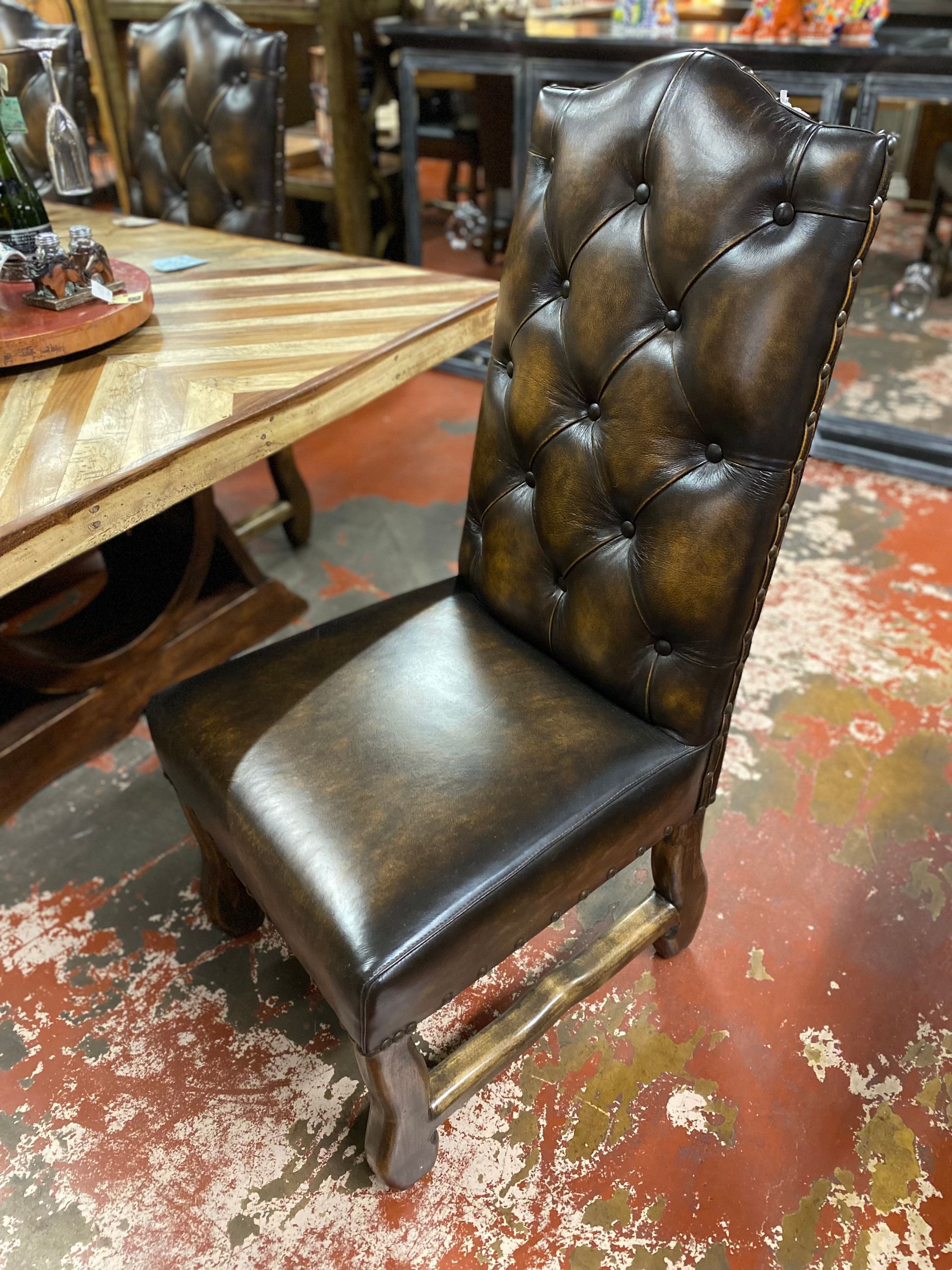 Dark brown leather tufted dining chair with wooden legs and back, next to a patterned wooden table in a showroom.