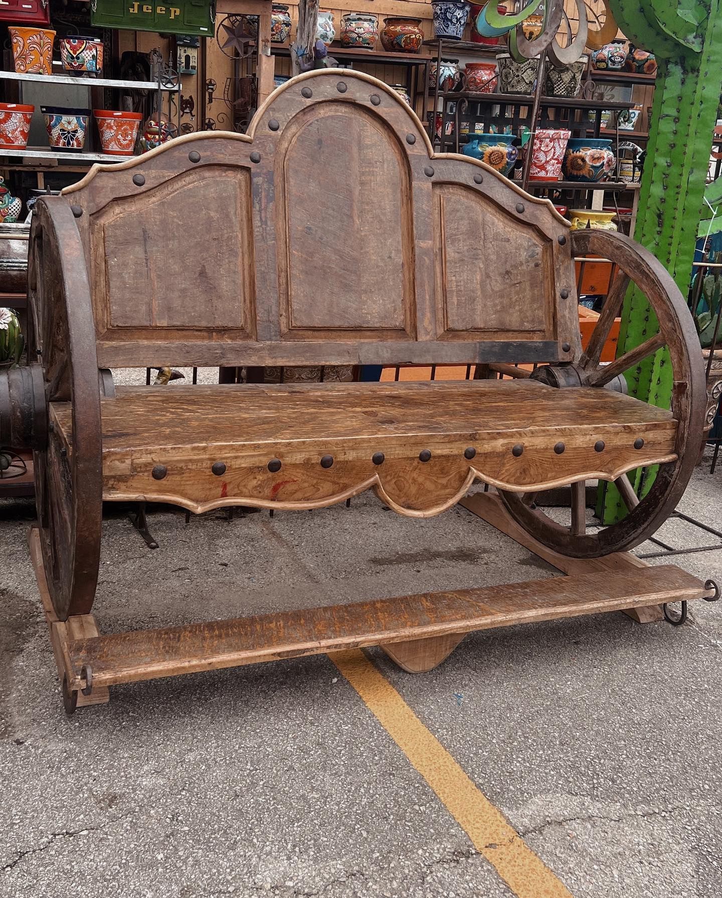 Wooden bench made to look like a wagon, with wagon wheels and a backrest. The bench is brown and sits outside a shop.