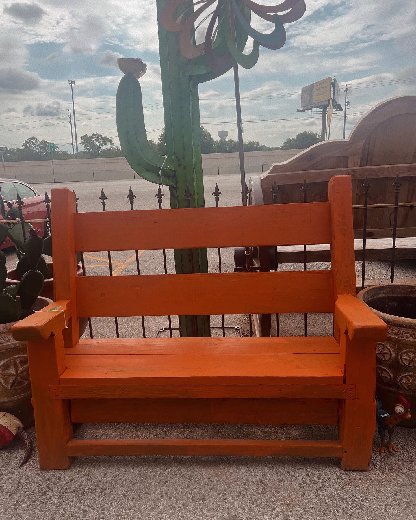 Orange wooden bench outdoors, with a cactus sculpture and other decorative elements in the background.