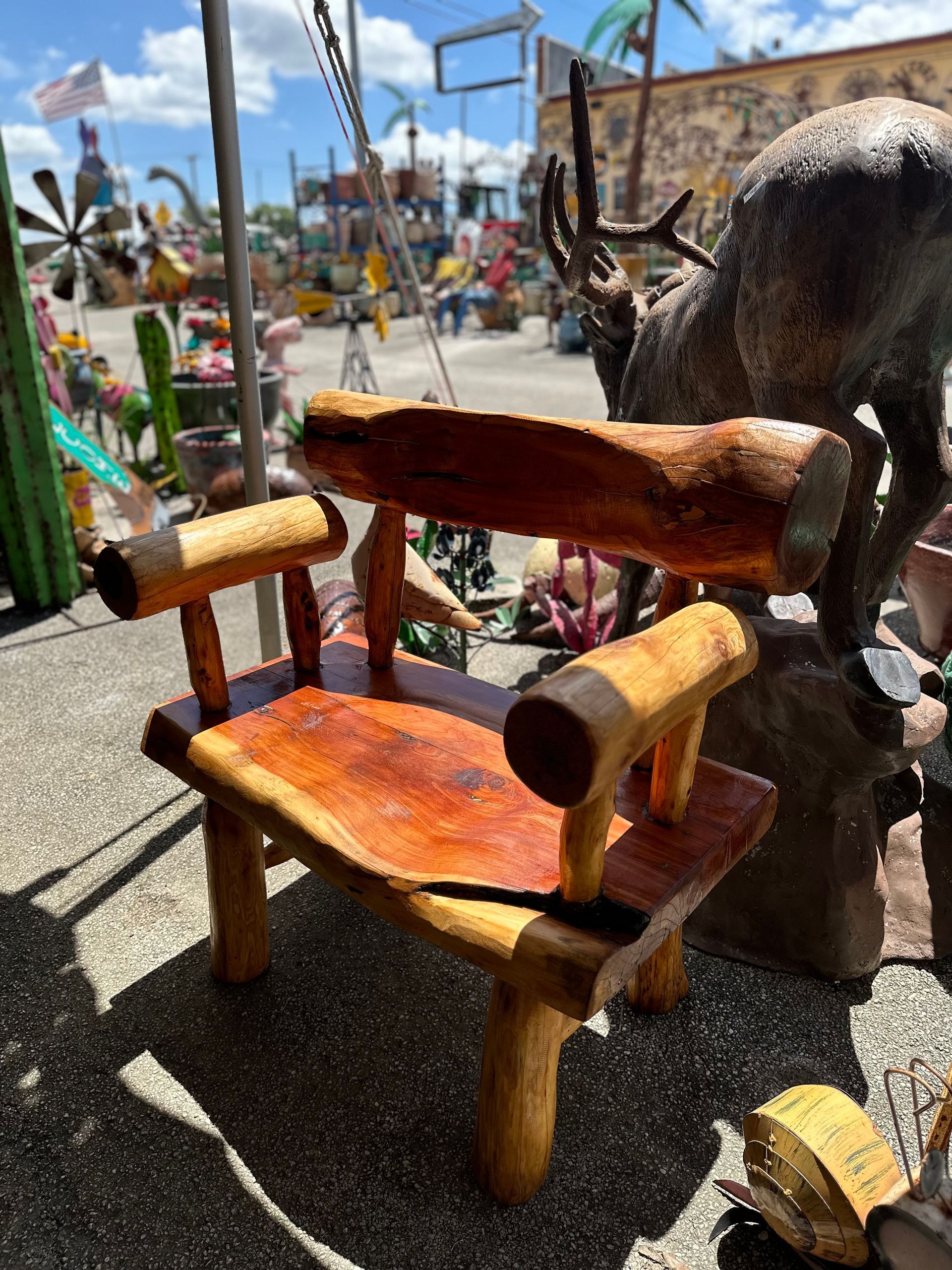 A handcrafted wooden chair with a rustic design sits outside. The chair is light brown and has natural log elements.