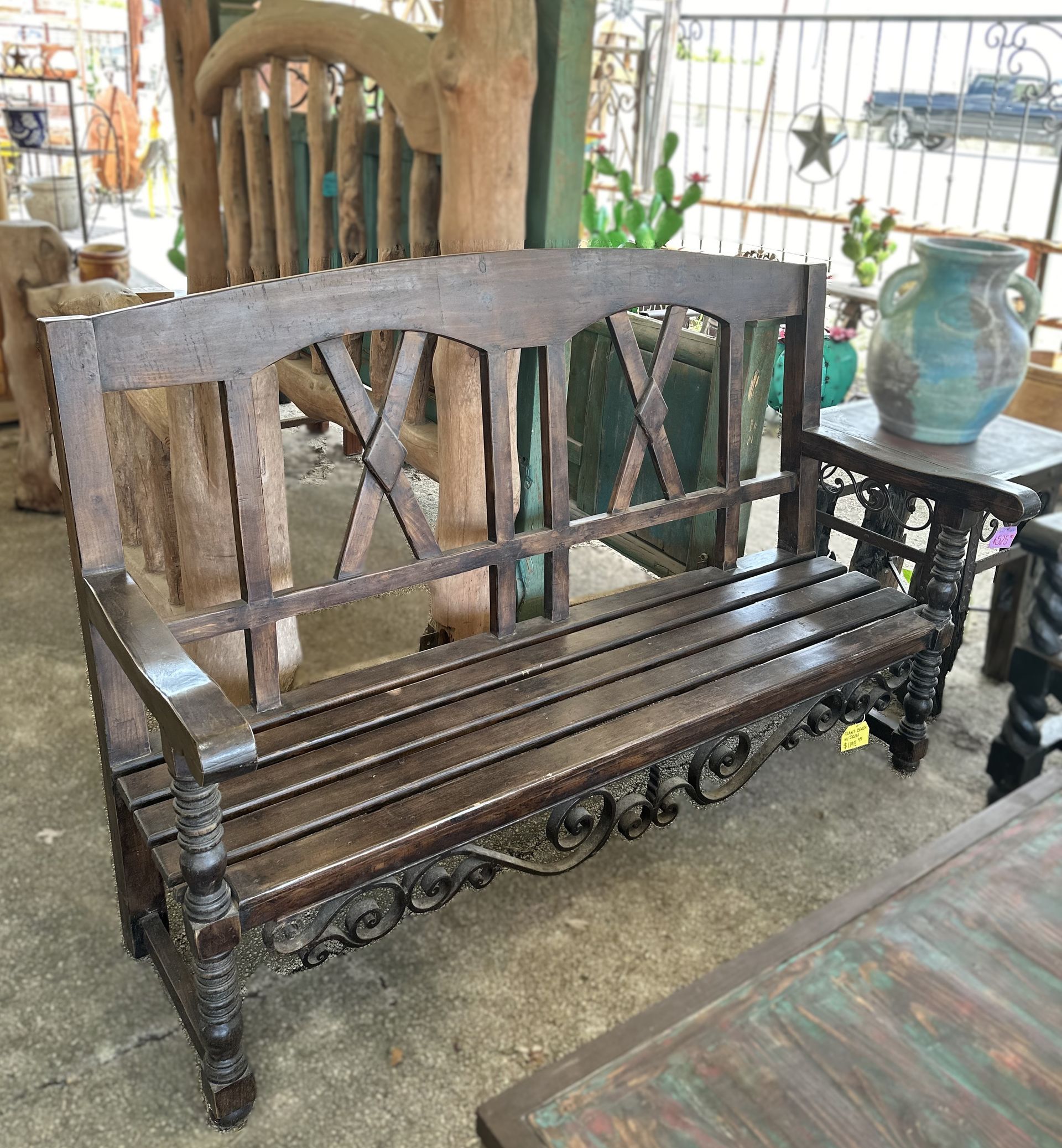 Wooden bench with dark brown finish and carved details, located outside in a garden setting.