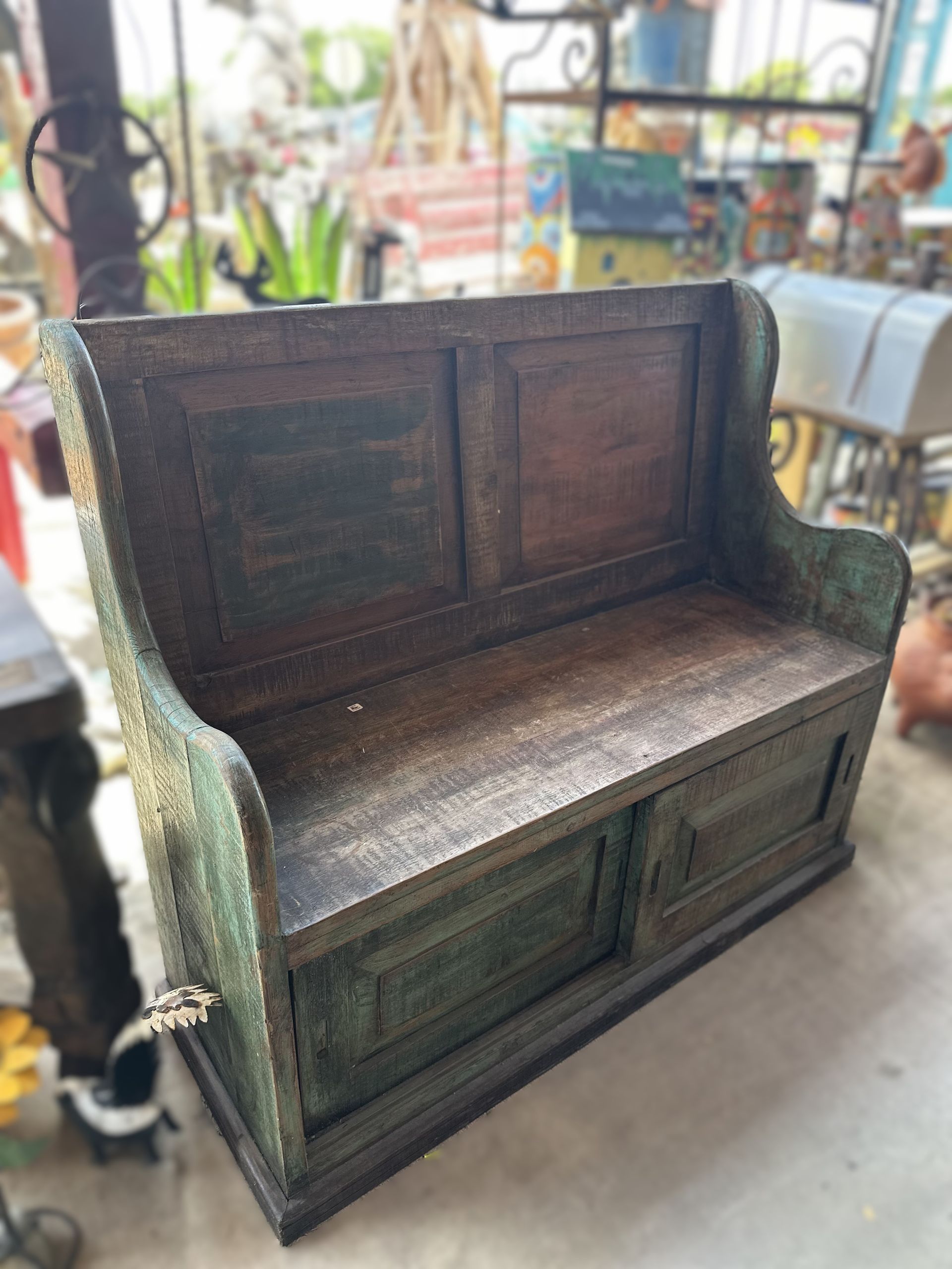 Wooden bench with storage, painted in green and brown tones, outdoors.
