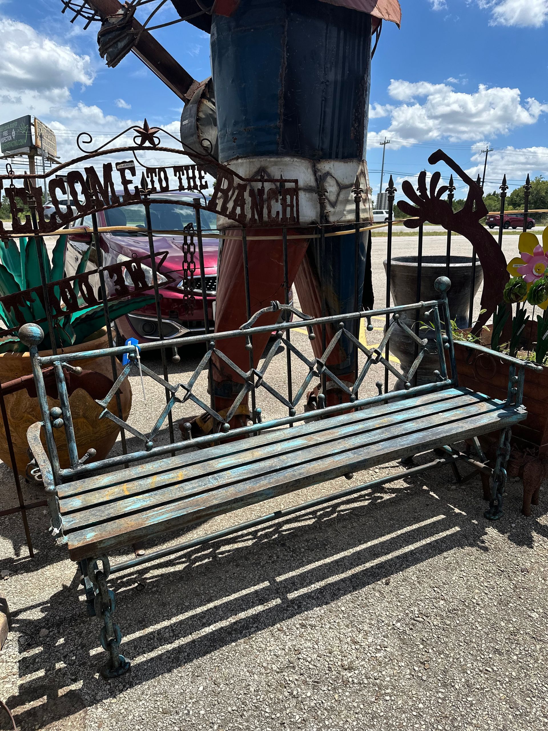 An ornate metal bench in front of a folk art sculpture of a person in a Texas flag-themed outfit, in an outdoor setting.