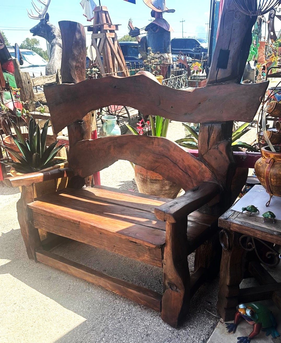 Wooden bench with a unique, organic design, set outside among crafts and plants.