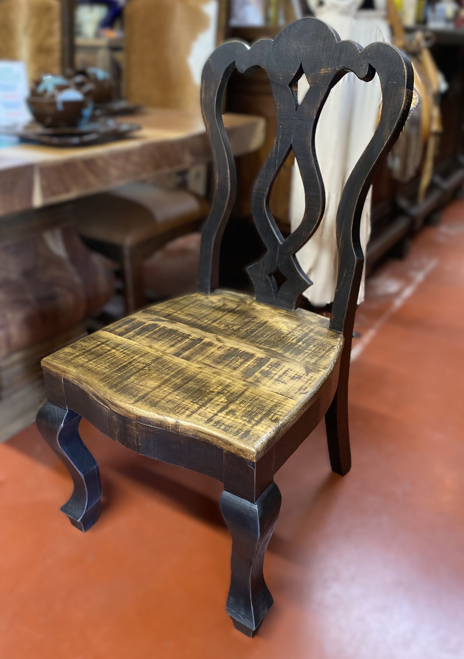A black wooden chair with a gold seat, ornate back, and curved legs sits on a red floor.