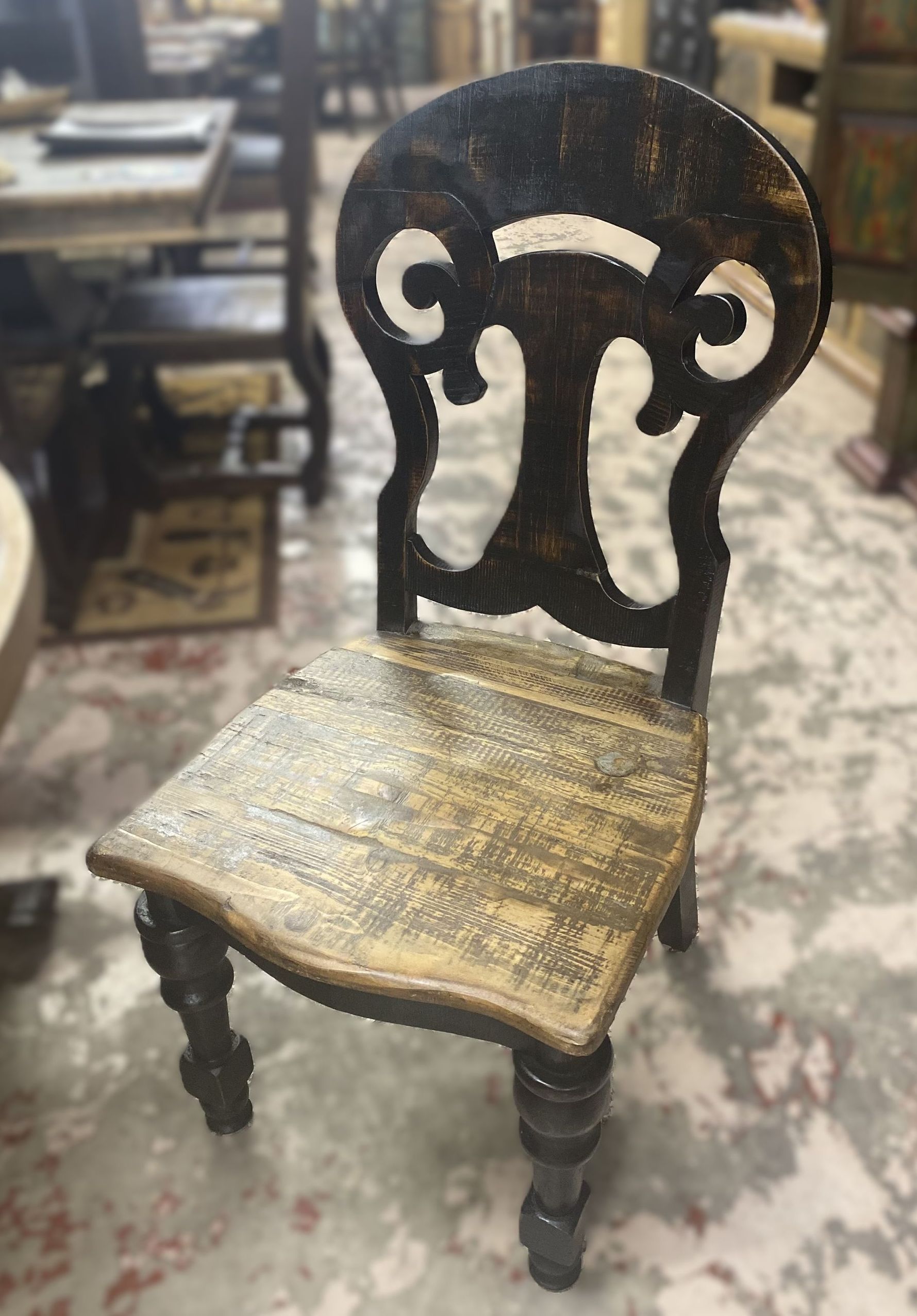 Ornate wooden chair with a carved back and a distressed, light-colored seat. The chair is in a room with other furniture.