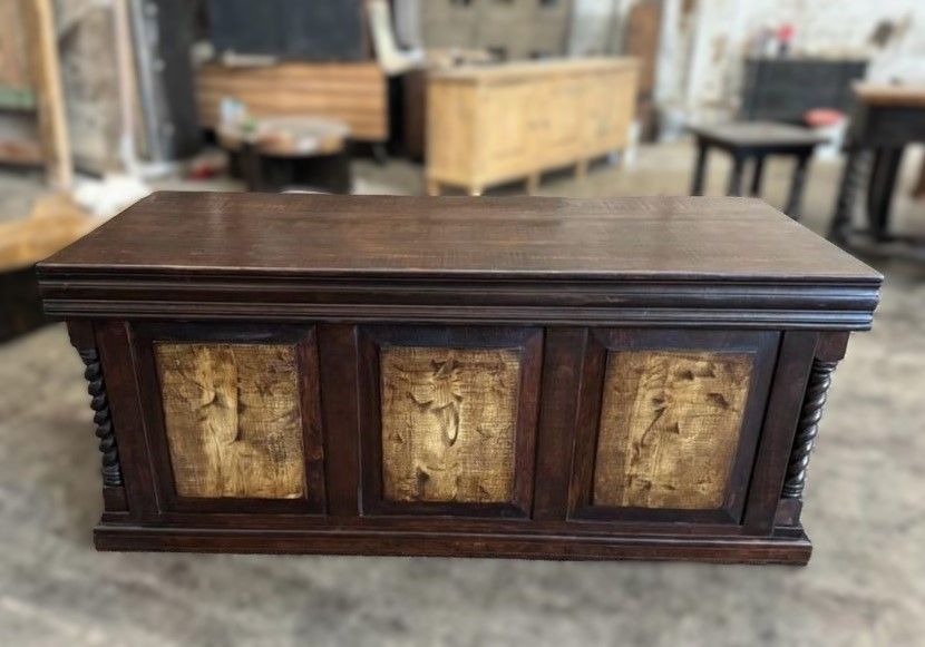A dark wooden cabinet with three decorative gold panels. The cabinet is in a workshop setting.