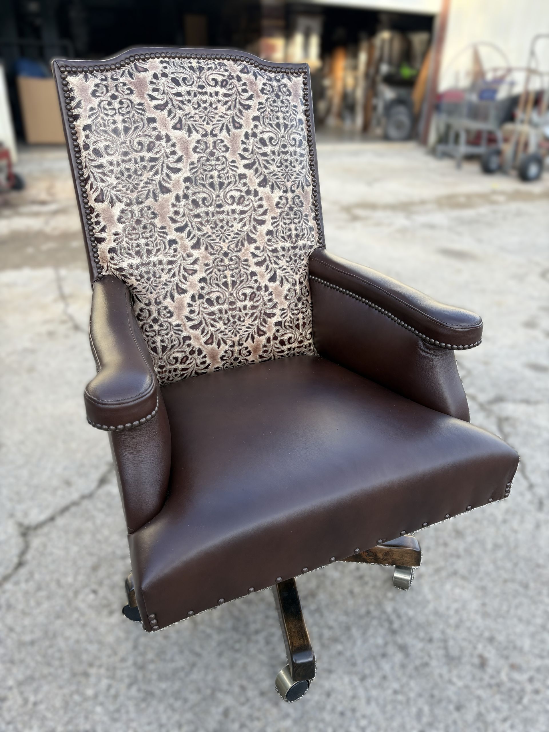 Brown leather office chair with a patterned back, set outdoors on concrete.