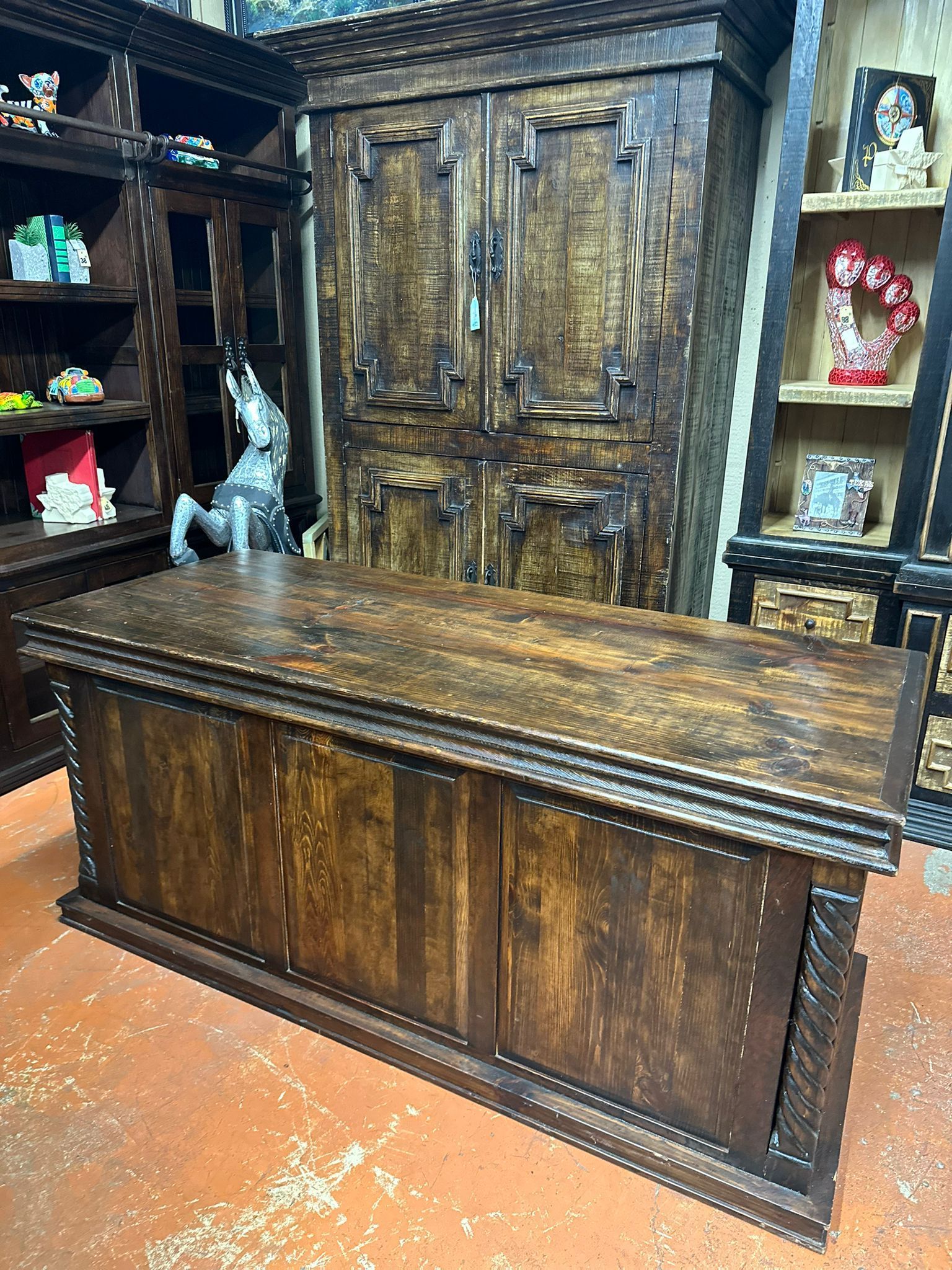 A dark wooden desk with ornate carvings in front of a large cabinet and shelves. The setting appears to be a furniture store.