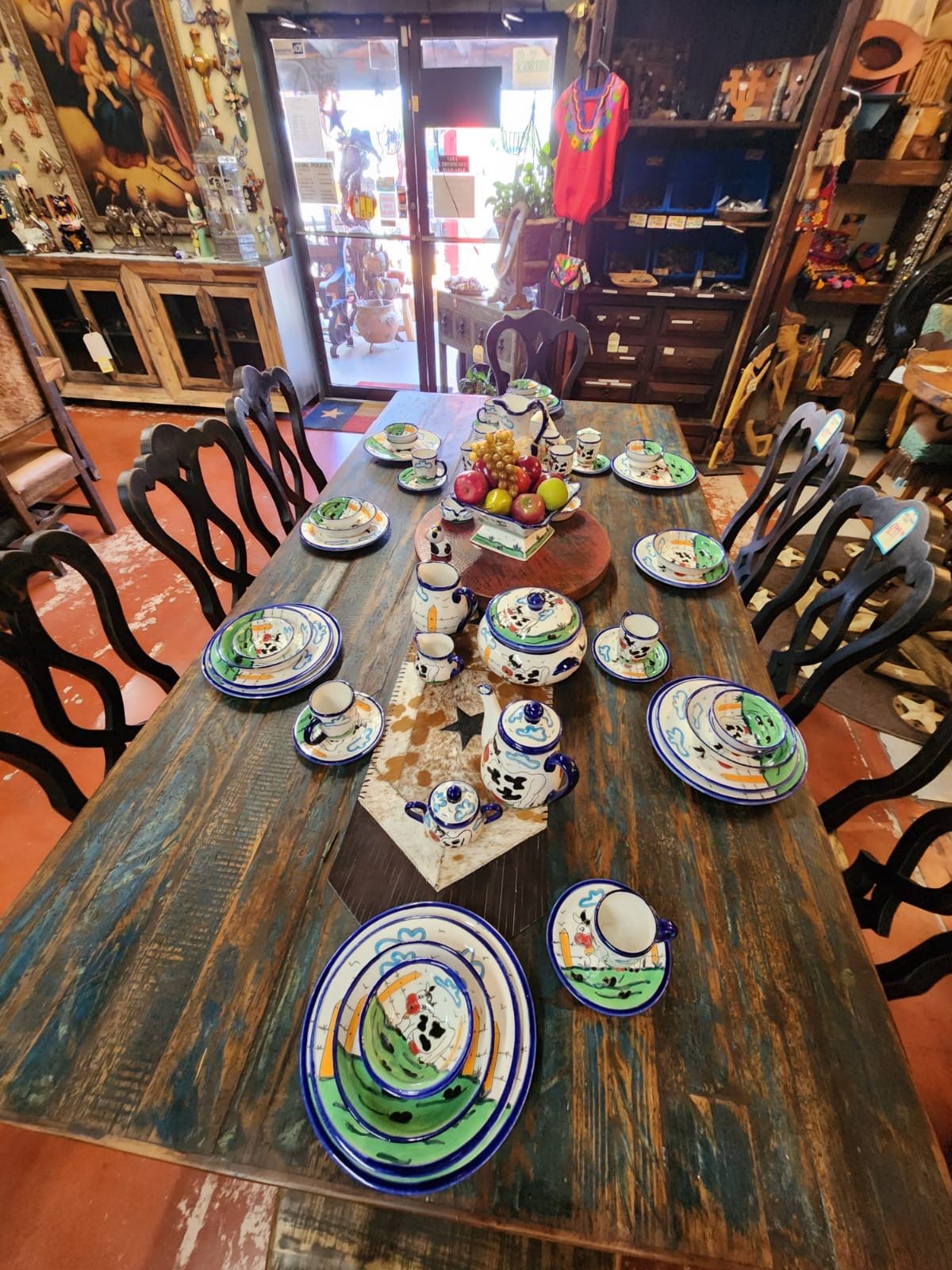 A wooden table set with colorful decorative plates, cups, and a teapot, possibly in a store.