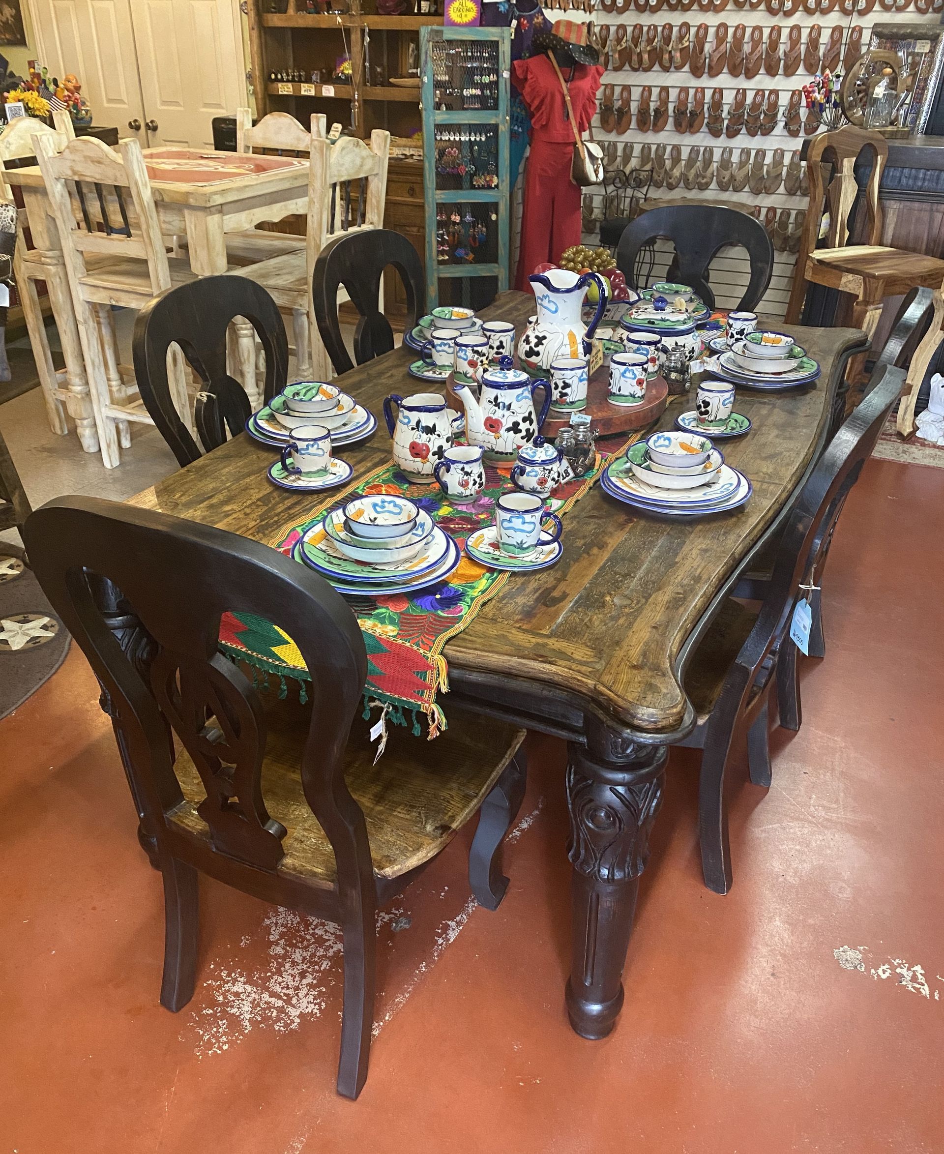 A dining table set for a meal, featuring colorful pottery, surrounded by ornate wooden chairs in a shop setting.