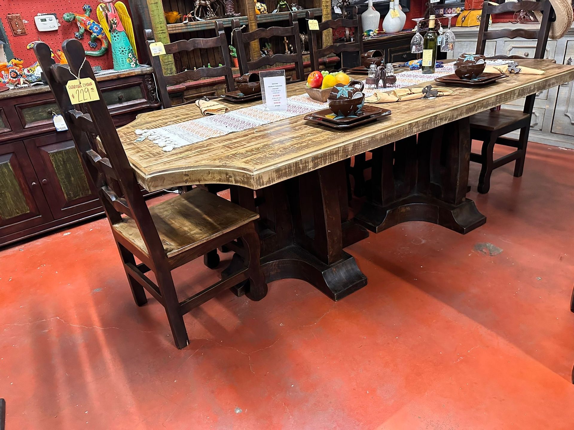Rustic wooden dining table and chairs in a cluttered room, with decorations and red flooring.