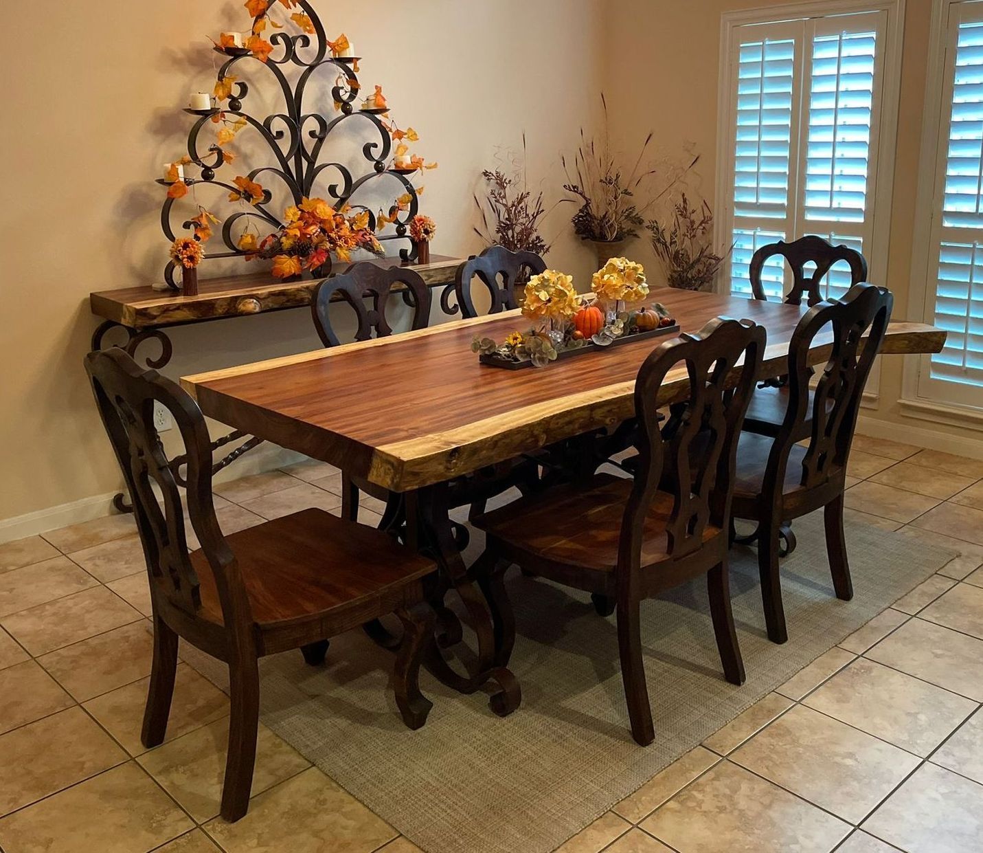 Dining room with a wooden table set for six, adorned with fall decorations and wooden chairs. A console table with a wrought iron decoration is against the wall.