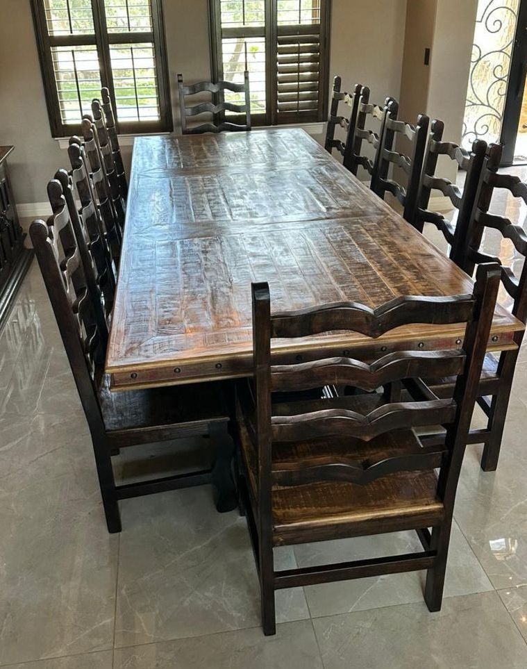 A large wooden dining table with many matching dark chairs, set in a room with windows.