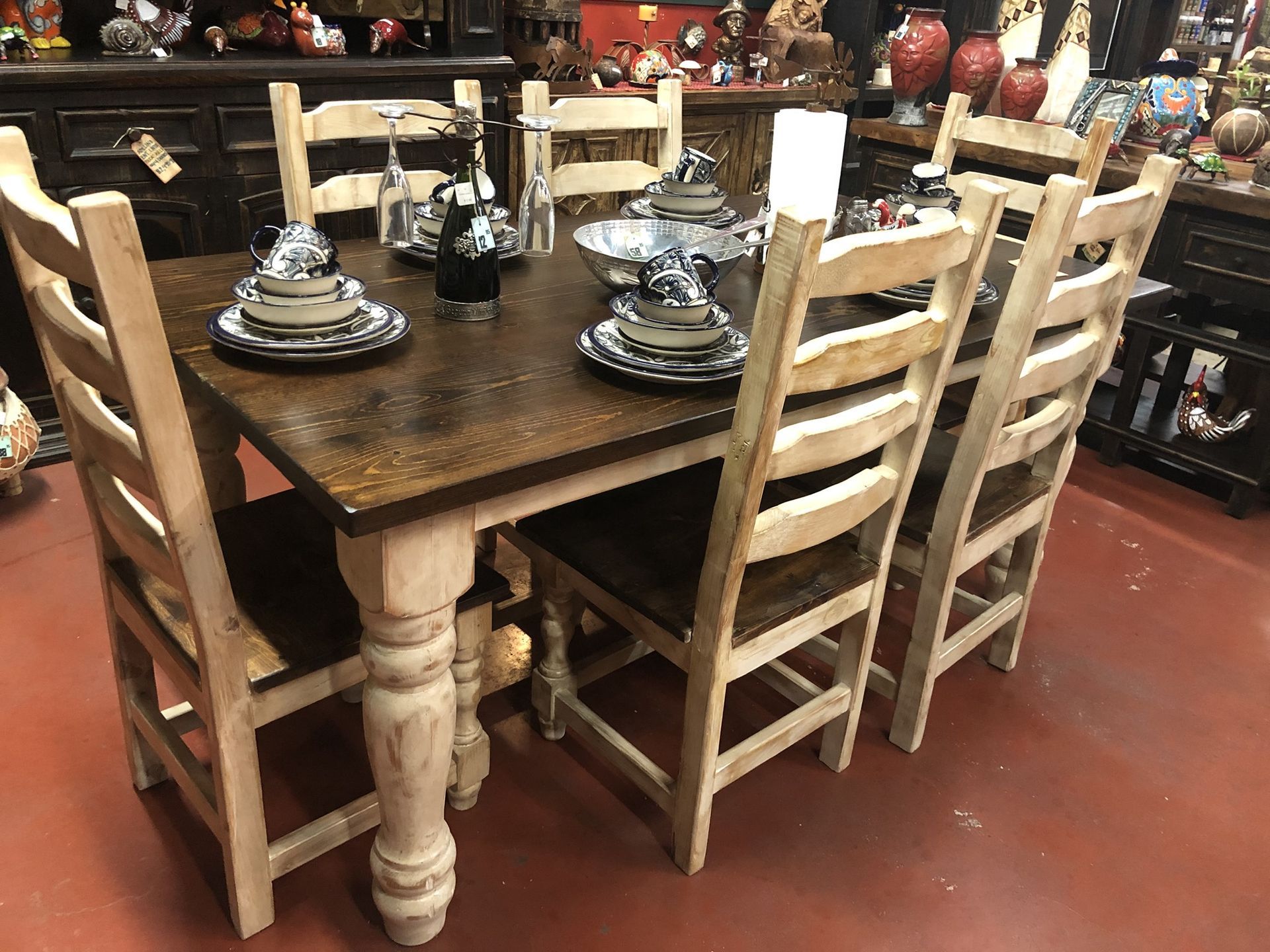 A rustic wooden dining table with six matching chairs set for a meal. The table is brown, and the chairs are light beige.