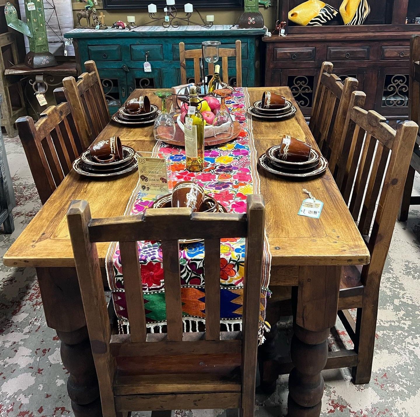 Wooden dining table set for six, with colorful patterned runner and place settings.  Chairs and sideboard with folk decor are visible in the background.
